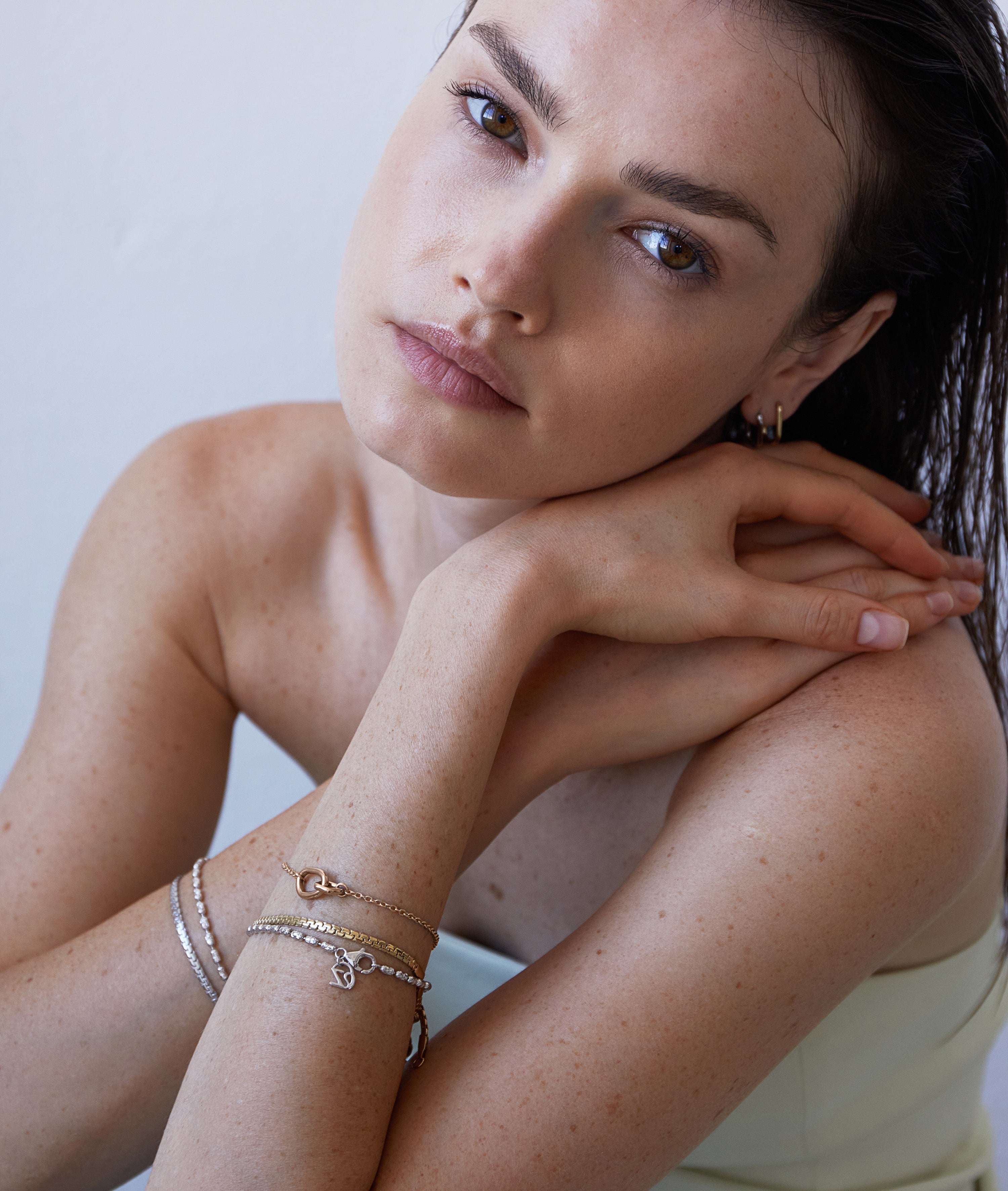 Eine Frau mit Sommersprossen stützt ihr Kinn auf ihre Hände, trägt das Echtzeit Armband - Like Diamonds von Echtzeit und blickt ruhig in die Kamera - ein perfektes Beispiel für zeitlosen Damenschmuck.
