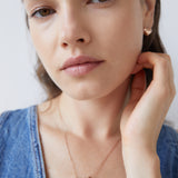 Frau trägt Echtzeit Ohrstecker - Puffy Heart von Echtzeit und ein Denim-Top, berührt ihr Gesicht und blickt sanft in die Kamera - ein Look mit zeitloser Eleganz und romantischer Note.