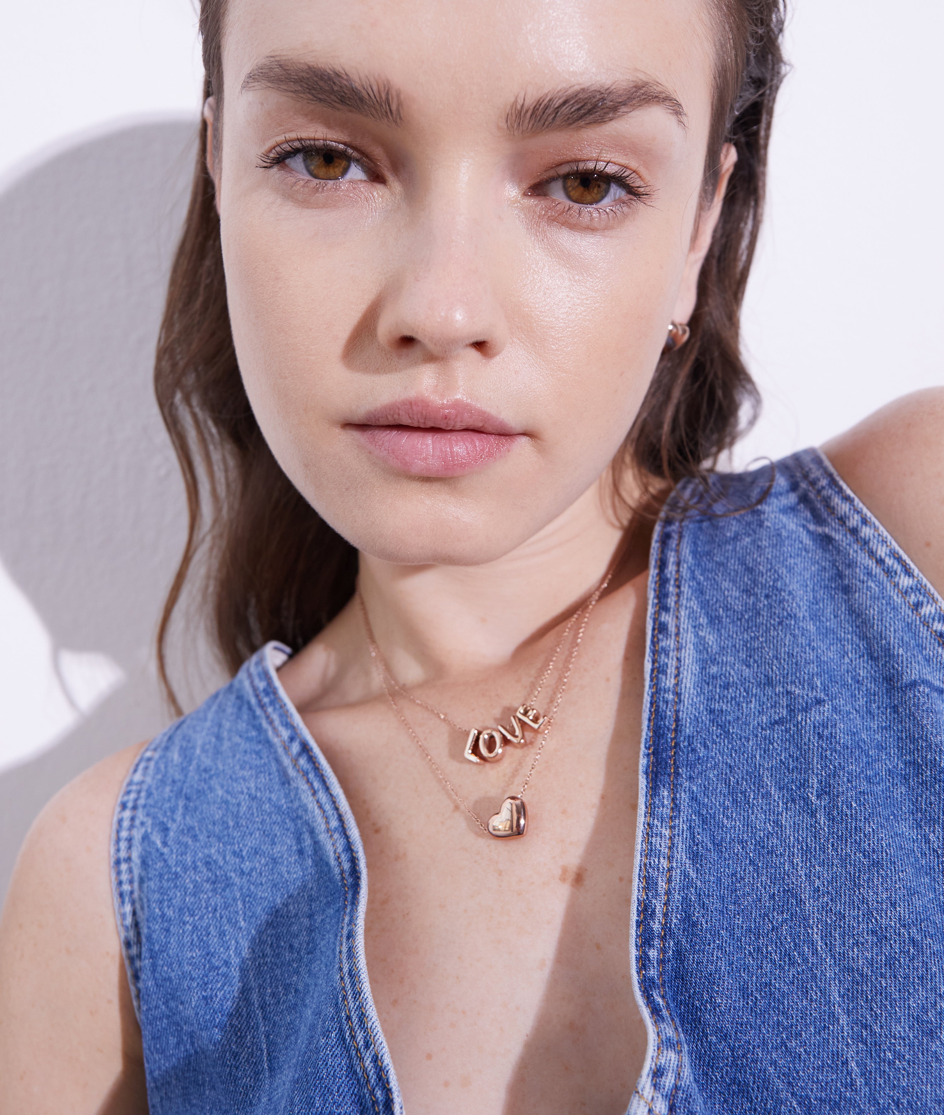 Eine Frau in einem Denim-Top stylt mehrlagige Goldketten mit der Echtzeit Halskette - Love Letters by Echtzeit und einem Herzanhänger - ein ideales modisches Accessoire für jeden Look.