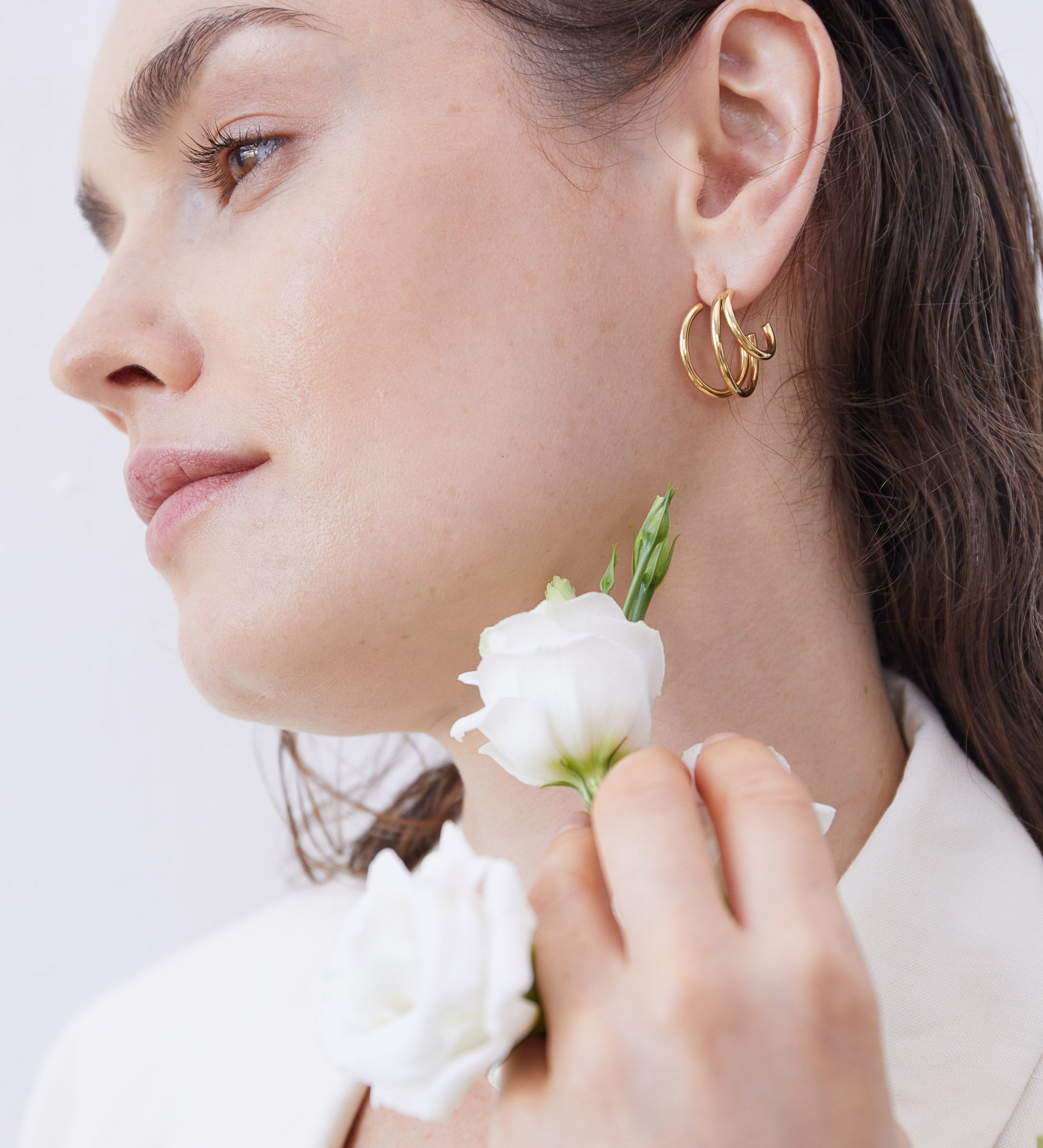 Frau mit goldenen Creolen und weißen Blüten in der Hand – zarter, natürlicher Look mit elegantem Schmuck-Statement.