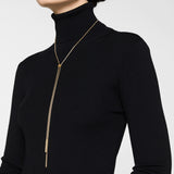 Eine Frau mit schwarzem Rollkragen trägt die LIEBESKIND BERLIN Halskette - The Everyday Combination von Liebeskind Berlin, eine lange goldene Halskette mit einem Y-förmigen Tropfen-Anhänger.