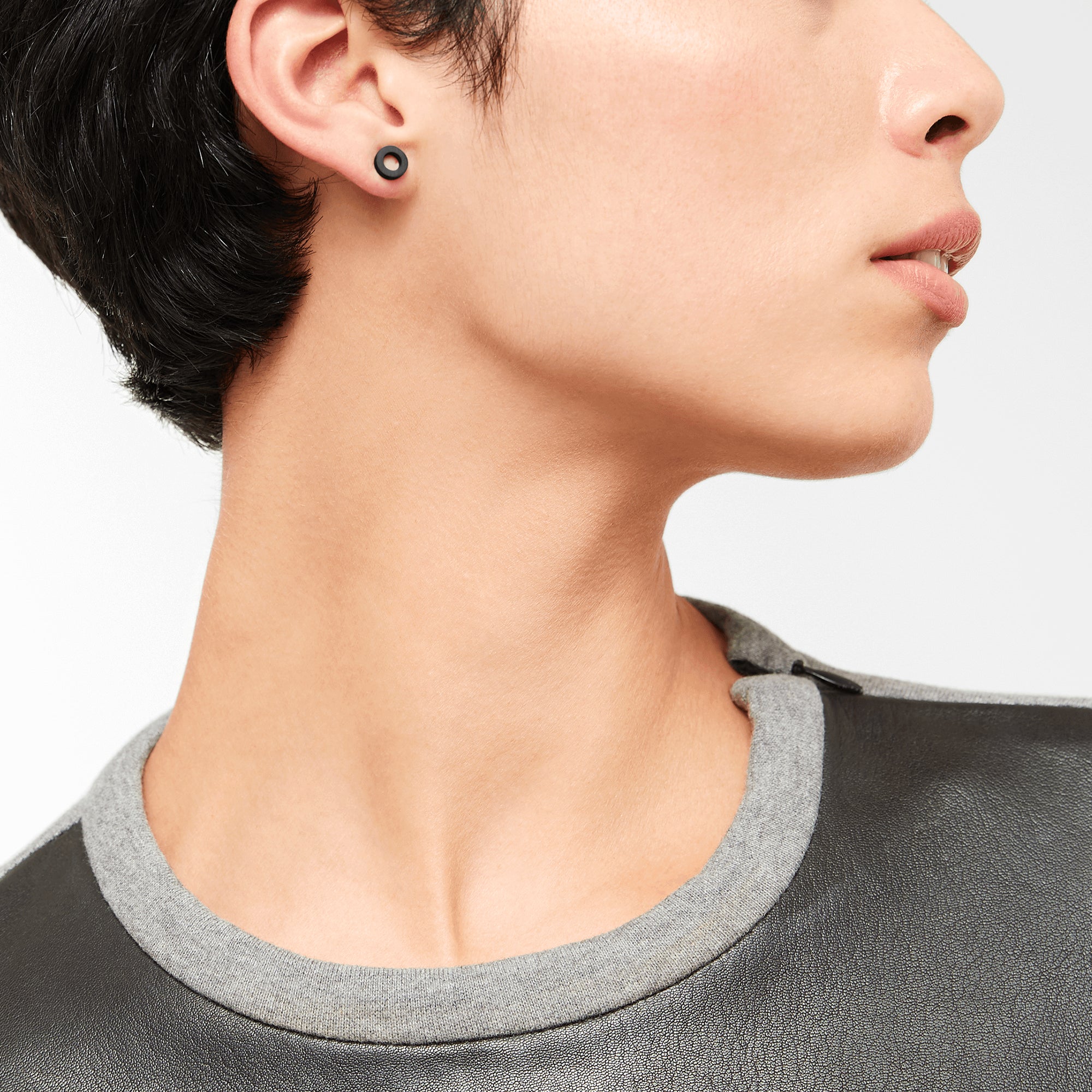 Person mit kurzen dunklen Haaren, in einem grauen lederbesetzten Hemd, seitwärts blickend, trägt LIEBESKIND BERLIN Ohrstecker - The Geometric von Liebeskind Berlin.