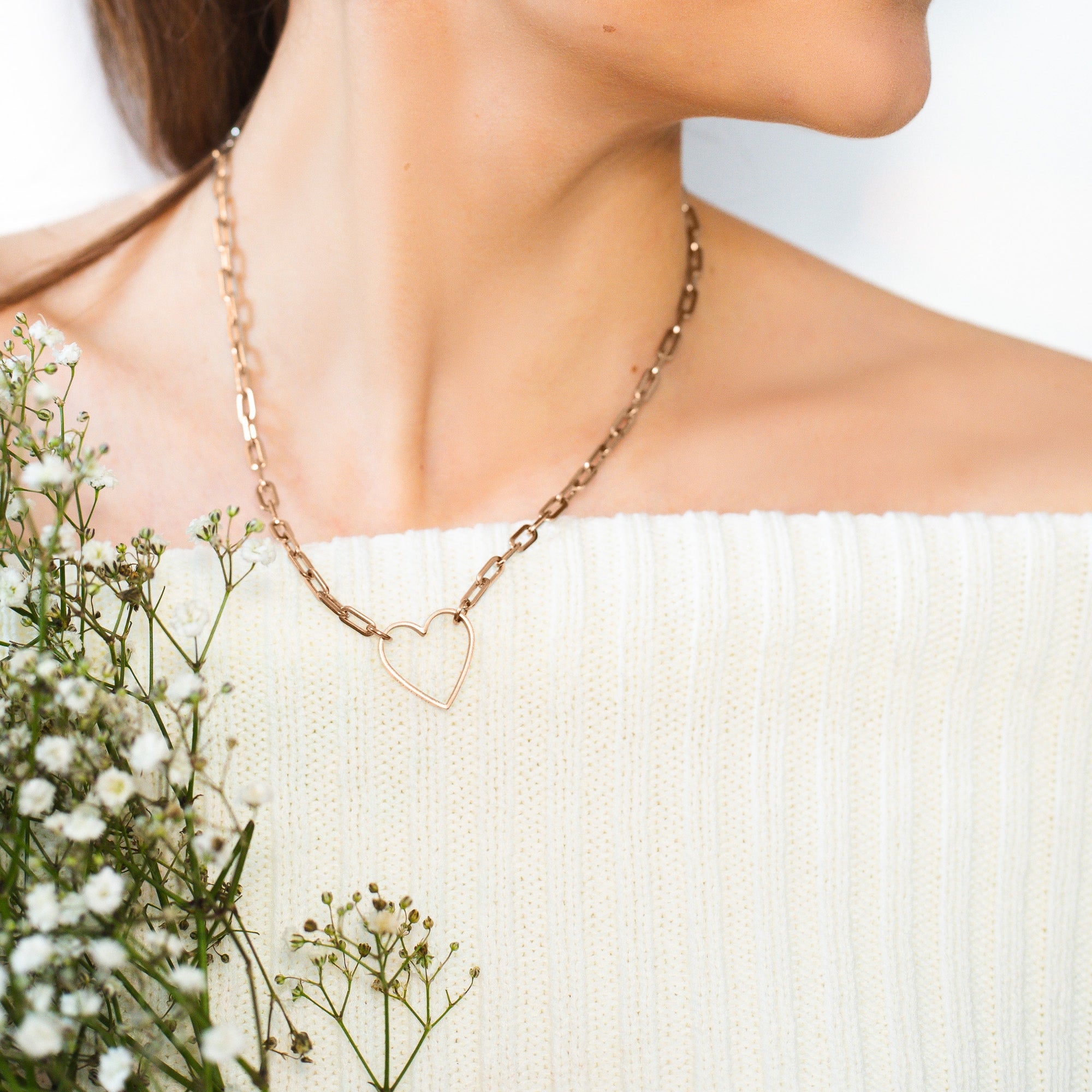 Frau trägt die goldene Halskette LIEBESKIND BERLIN - in Liebe und ein weißes schulterfreies Oberteil mit weißen Blumen - ein ideales, durchdachtes Geschenk von Liebeskind Berlin.