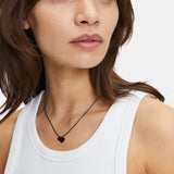Eine Frau in einem weißen Tank-Top trägt die schwarze Liebeskind Berlin Classy Heart Halskette, die ihrem Look einen modernen Touch verleiht.