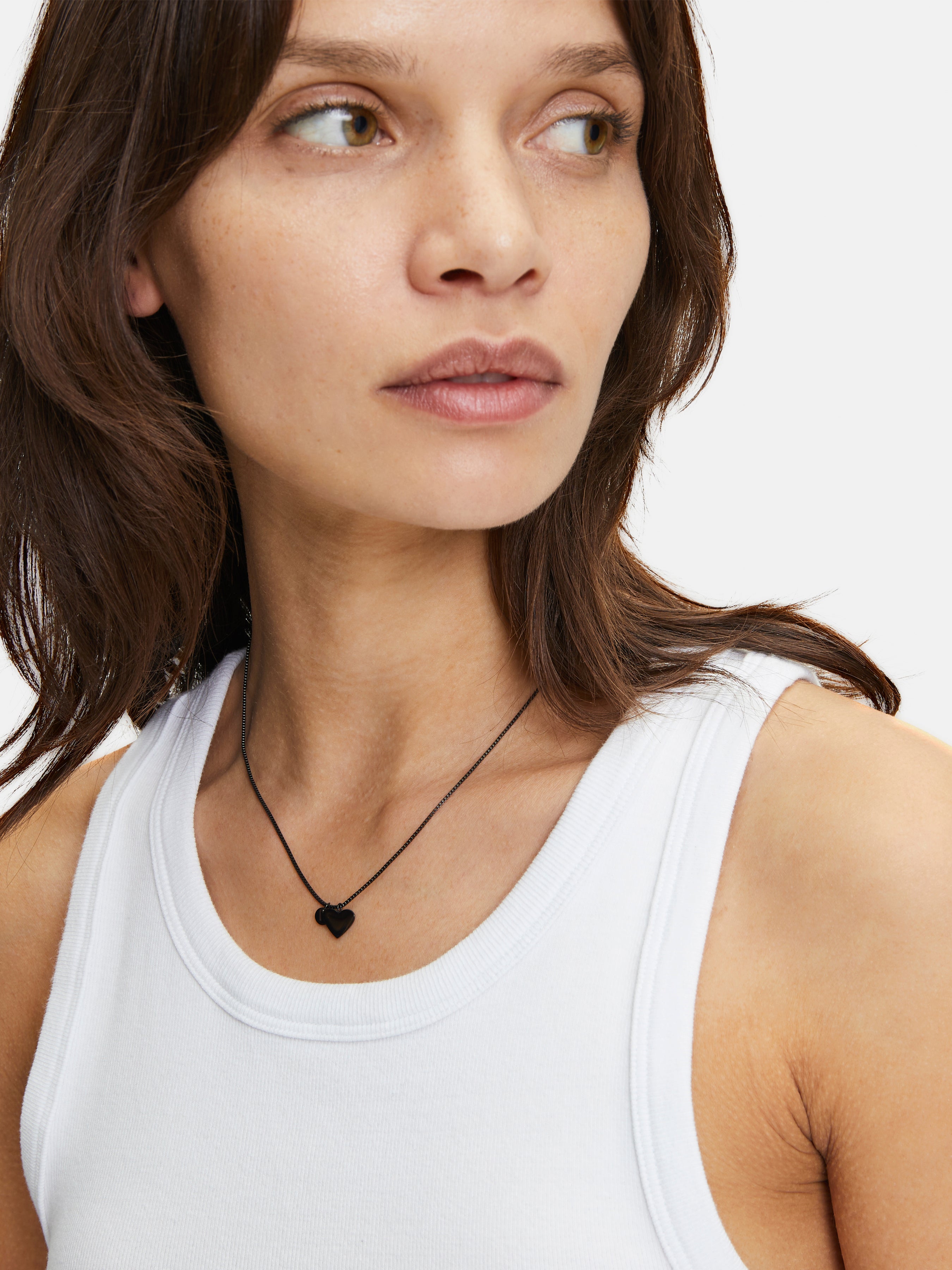 Eine Frau in einem weißen Tank-Top trägt die schwarze Liebeskind Berlin Classy Heart Halskette, die ihrem Look einen modernen Touch verleiht.
