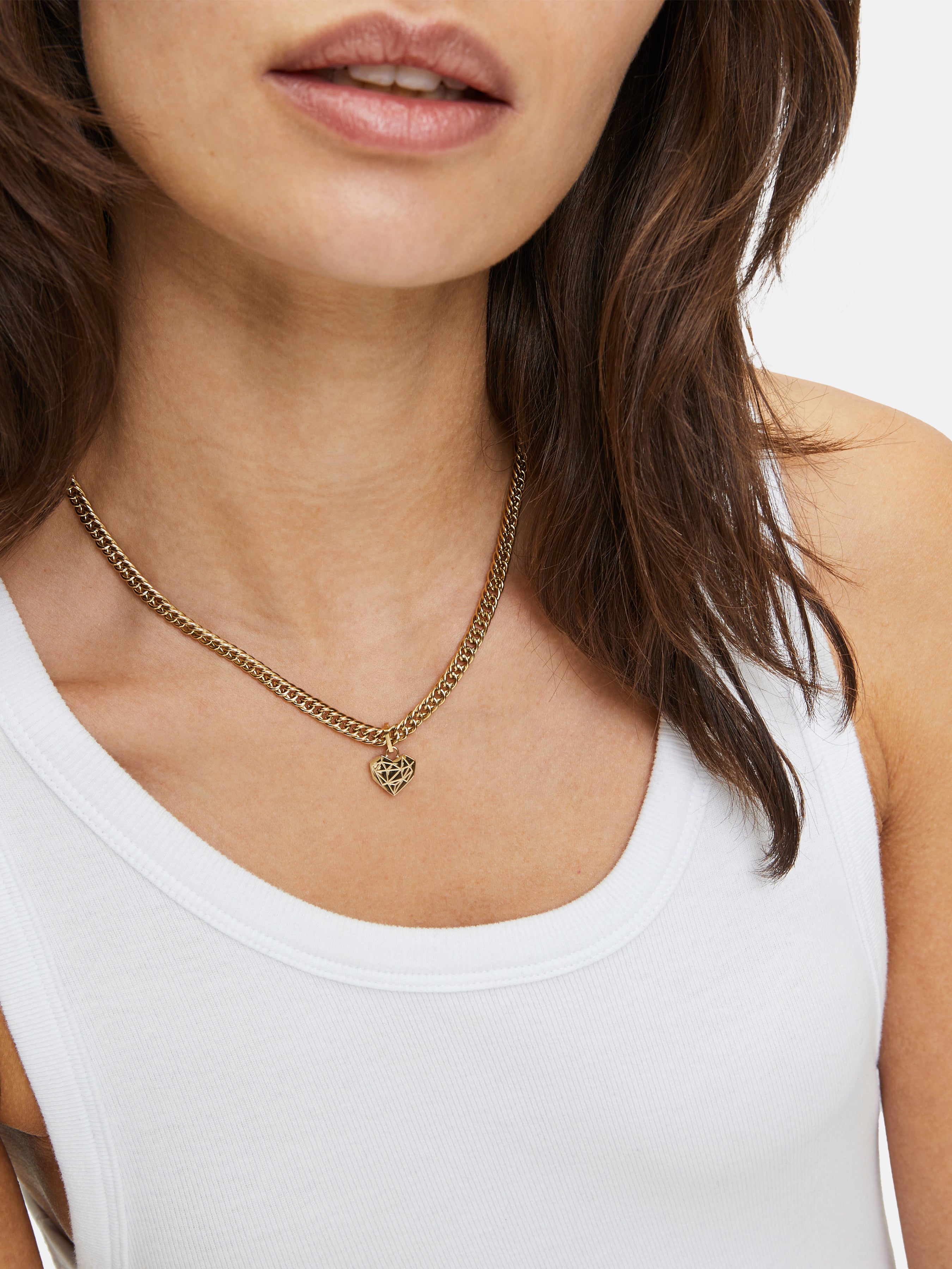 Frau trägt ein weißes Tank-Top und die LIEBESKIND BERLIN Halskette - Broken Heart Chunky von Liebeskind Berlin, die eine klobige Goldkette mit einem herzförmigen Anhänger aufweist.