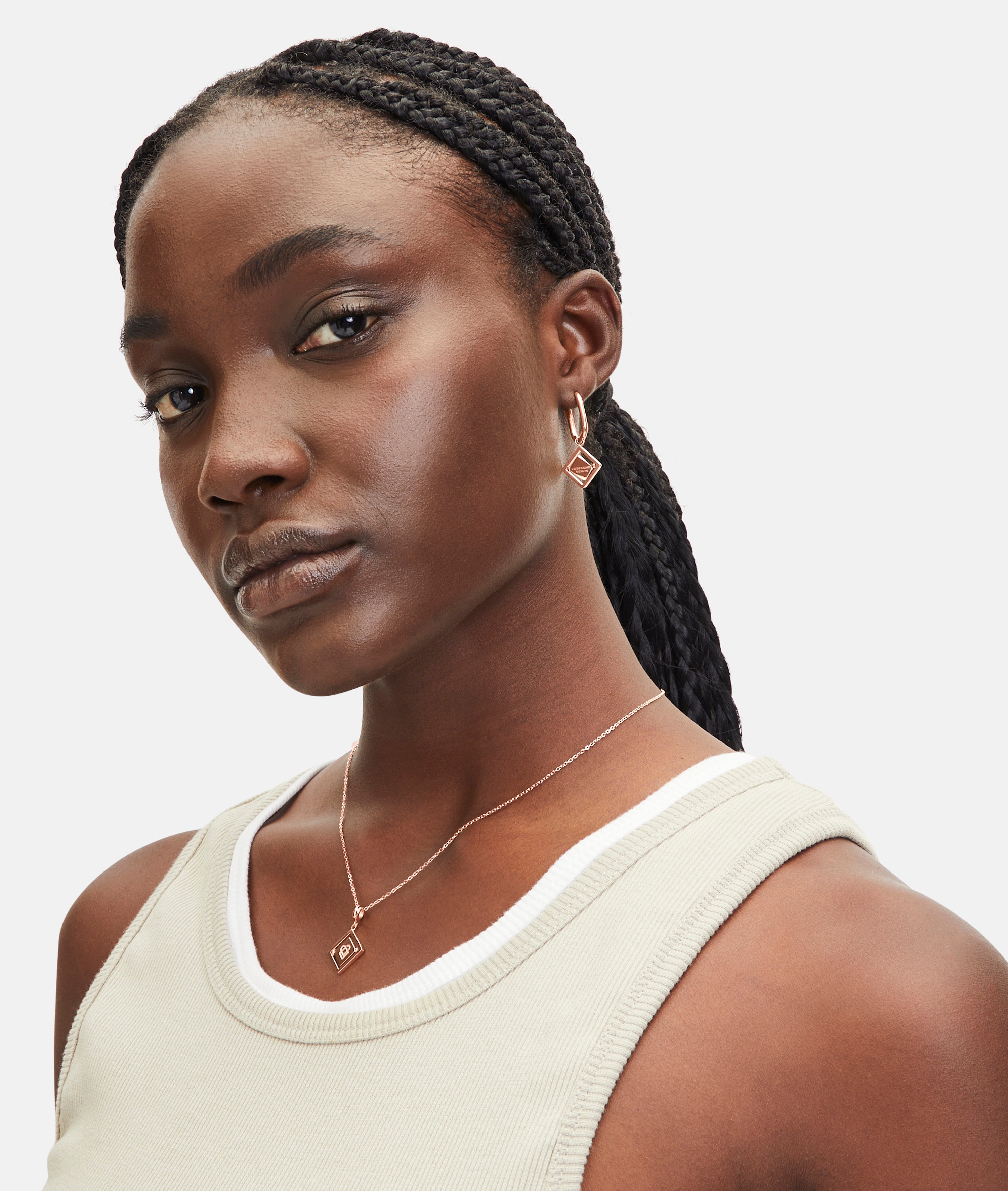 Eine Frau mit geflochtenen Haaren trägt geometrische goldene Ohrringe und die LIEBESKIND BERLIN Halskette - Swinging Icon von Liebeskind Berlin, gepaart mit einem leichten Tanktop für einen mühelos eleganten Look.