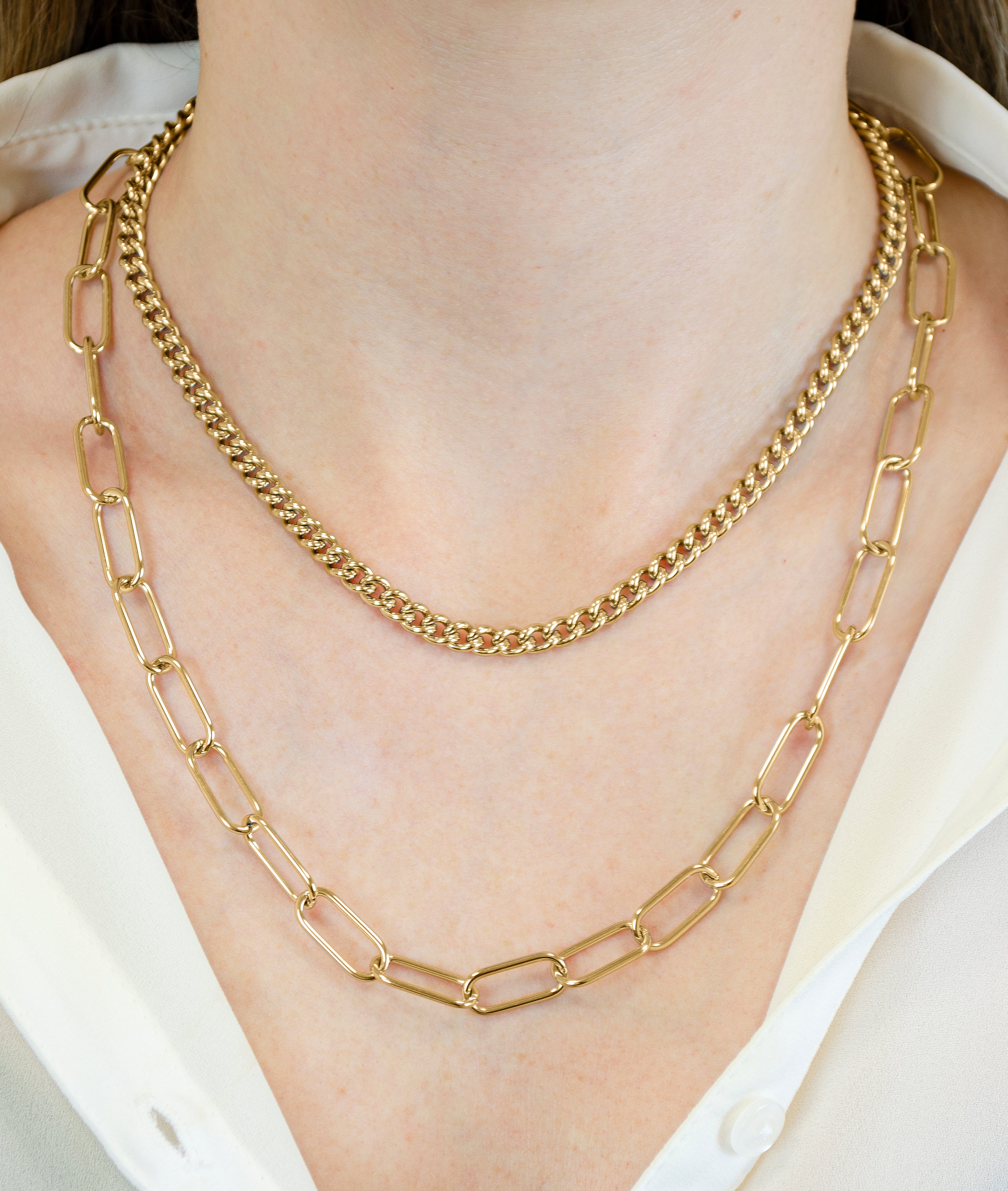 Das LIEBESKIND BERLIN Halsketten-Set - The Layering von Liebeskind Berlin, bestehend aus goldenen Ketten mit kleinen und großen Gliedern, wird elegant über ein weißes Hemd gestylt.