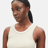 Eine Frau in einem beigen Tank-Top mit geflochtenen Haaren schaut zur Seite und trägt die LIEBESKIND BERLIN Halskette - The Love Lock. Diese elegante Halskette aus Edelstahl von Liebeskind Berlin ist ein dezentes Accessoire, perfekt als Geschenk Liebe.