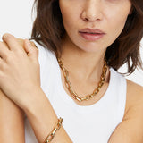 Frau in einem weißen Tank-Top trägt das LIEBESKIND BERLIN Armband - The Secure Tag von Liebeskind Berlin, gepaart mit einer goldenen Halskette. Ideal für Damen Schmuck Fans, die mühelose Eleganz schätzen.