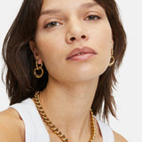 Frau trägt ein weißes Tanktop, goldene Ohrringe und die LIEBESKIND BERLIN Halskette - The Organic von Liebeskind Berlin und schaut in die Kamera.