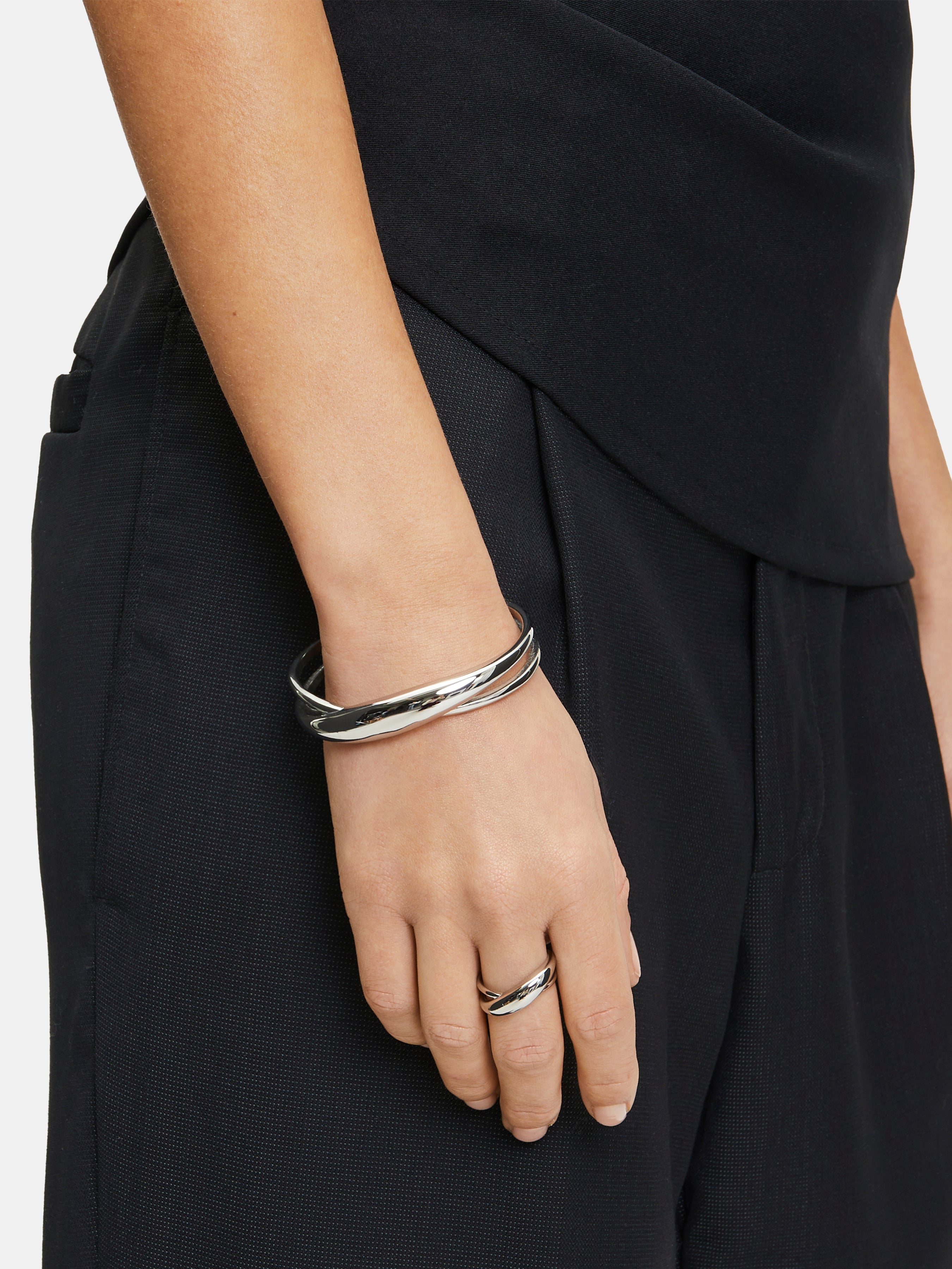 Eine Person, die den Liebeskind Berlin Armreif - The Organic Twist und einen dazu passenden Ring trägt, gekleidet in Schwarz.
