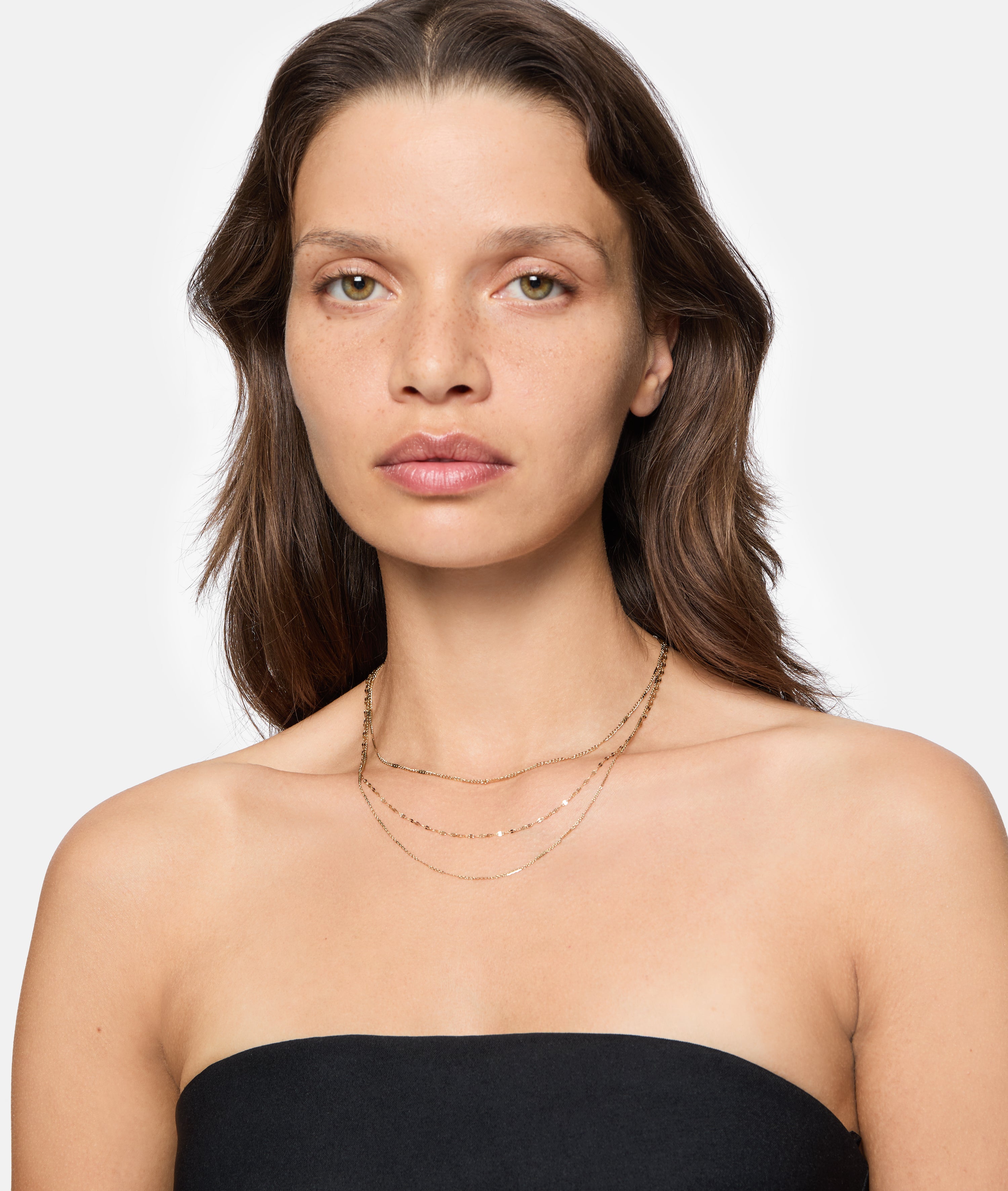 Eine Frau mit hellbraunem Haar trägt ein trägerloses schwarzes Oberteil und die LIEBESKIND BERLIN Halskette - Sparkling With Layers von Liebeskind Berlin, gestylt als elegantes Accessoire vor einem strahlend weißen Hintergrund.