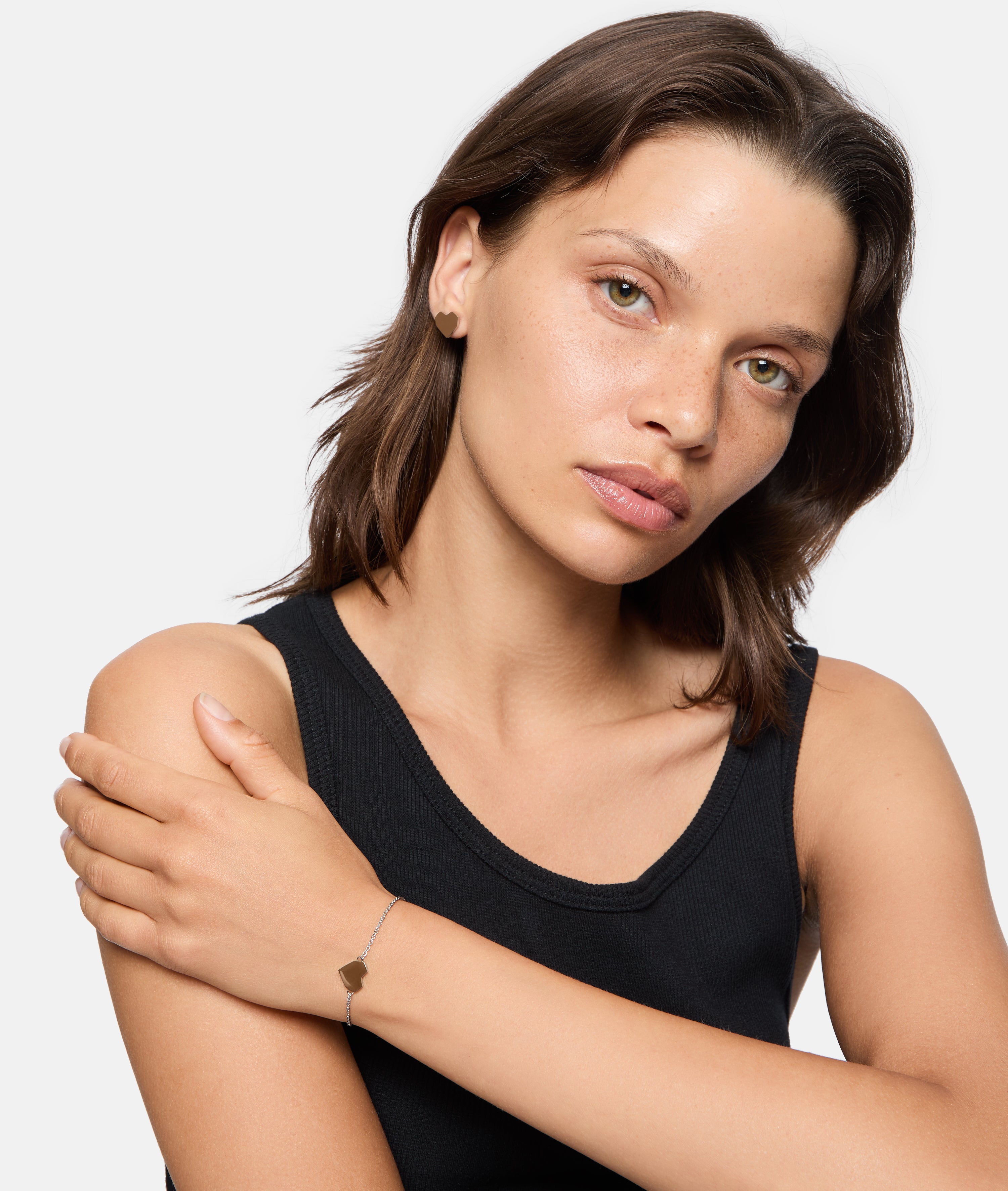 Eine Frau mit glattem braunem Haar in einem schwarzen ärmellosen Oberteil posiert mit einem gekreuzten Arm und trägt das LIEBESKIND BERLIN Armband - Urban Heart von Liebeskind Berlin.