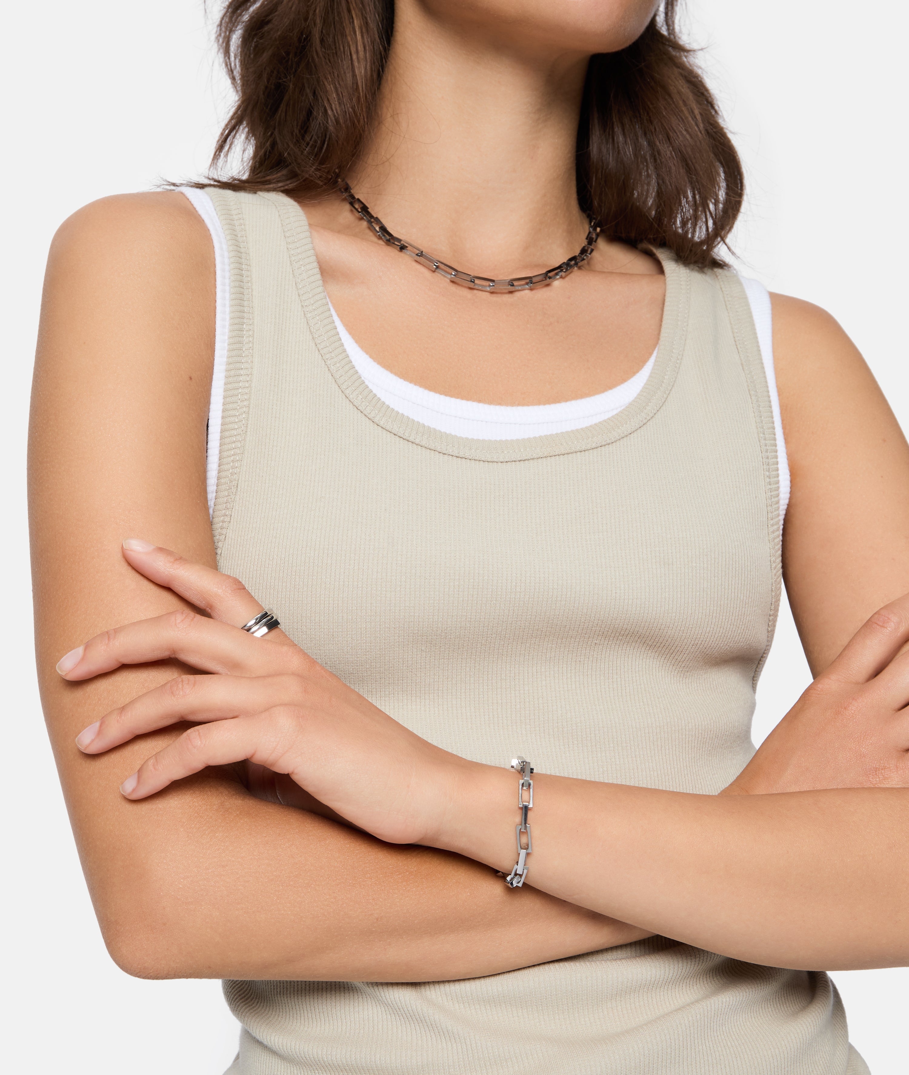 Frau in beigefarbenem Tank-Top verschränkt die Arme und trägt die Liebeskind Berlin Halskette - Urban Chic, zusammen mit einem Armband und einem Ring als Statement-Schmuck.