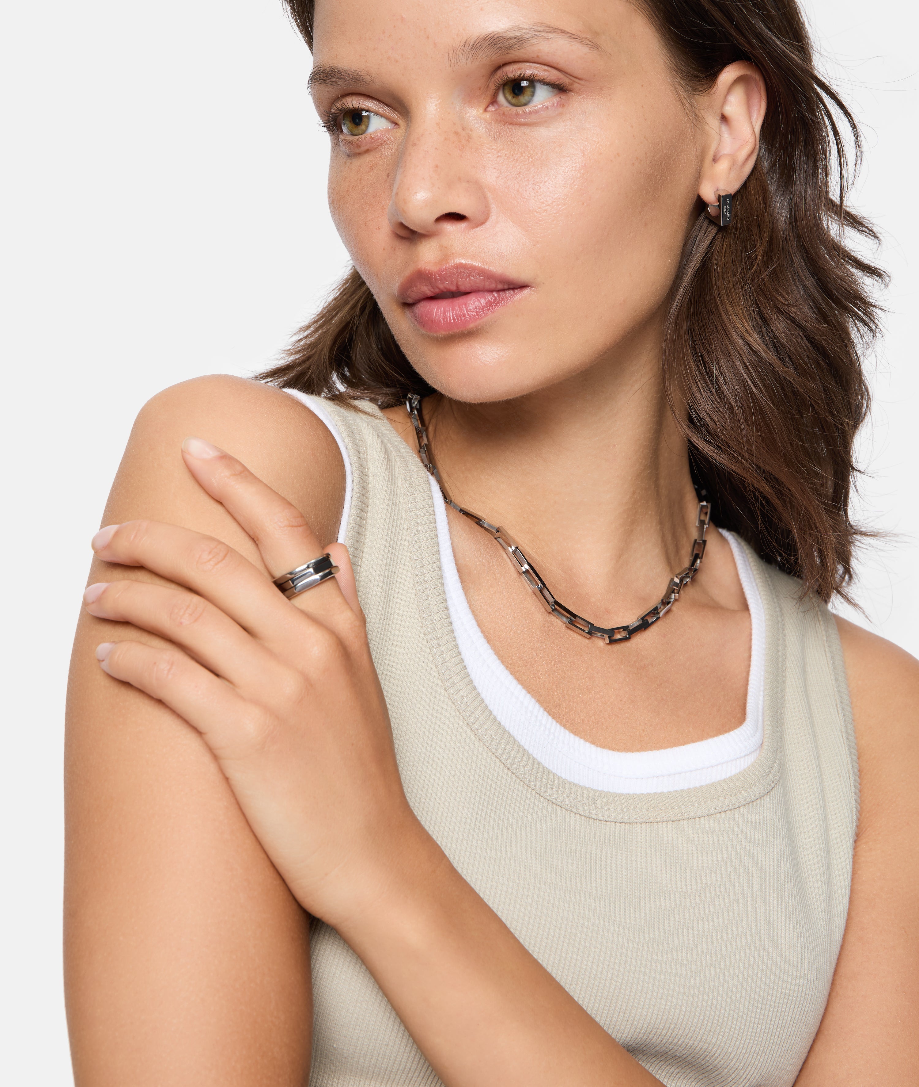 Frau in beigem Tank-Top mit silberner Halskette, Ring und LIEBESKIND BERLIN Creole - Urban Chic Statement Ohrringe von Liebeskind Berlin-einem eleganten Accessoire für Frauen, das zur Seite schaut.