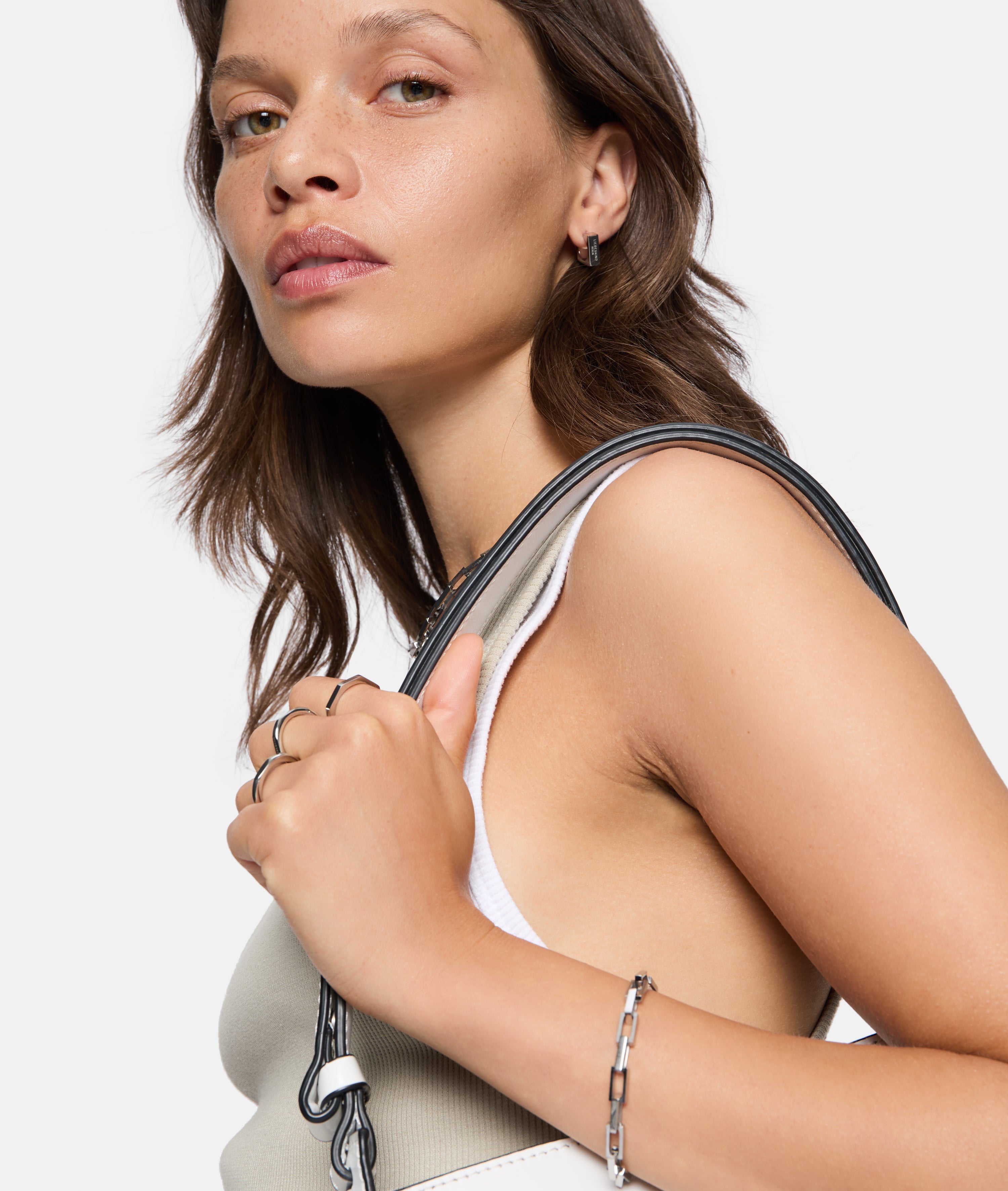 Frau mit gewelltem braunem Haar und Tanktop trägt LIEBESKIND BERLIN Creole - Urban Chic Ohrringe und hält einen Taschenriemen über der Schulter - ein elegantes Accessoire von Liebeskind Berlin.