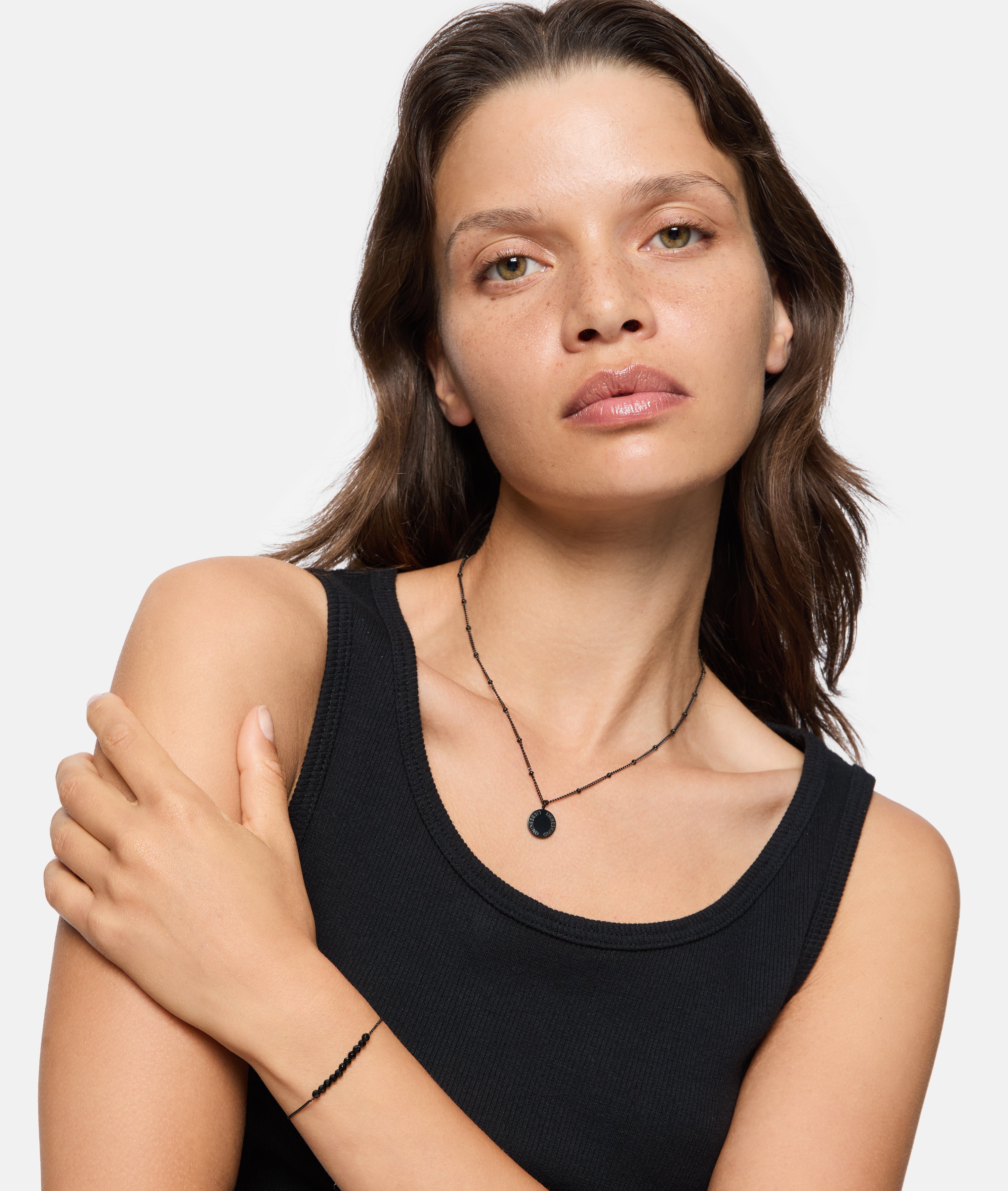 Frau mit hellbraunem Haar, schwarzem Tanktop und Halskette posiert mit einem gekreuzten Arm und trägt das Liebeskind Berlin Armband - Bead Mix.