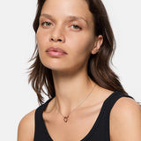 Frau mit mittelbraunem Haar in einem schwarzen Tanktop, die die LIEBESKIND BERLIN Halskette - The Organic Twist von Liebeskind Berlin für einen schicken Lagenlook trägt, schaut in die Kamera.