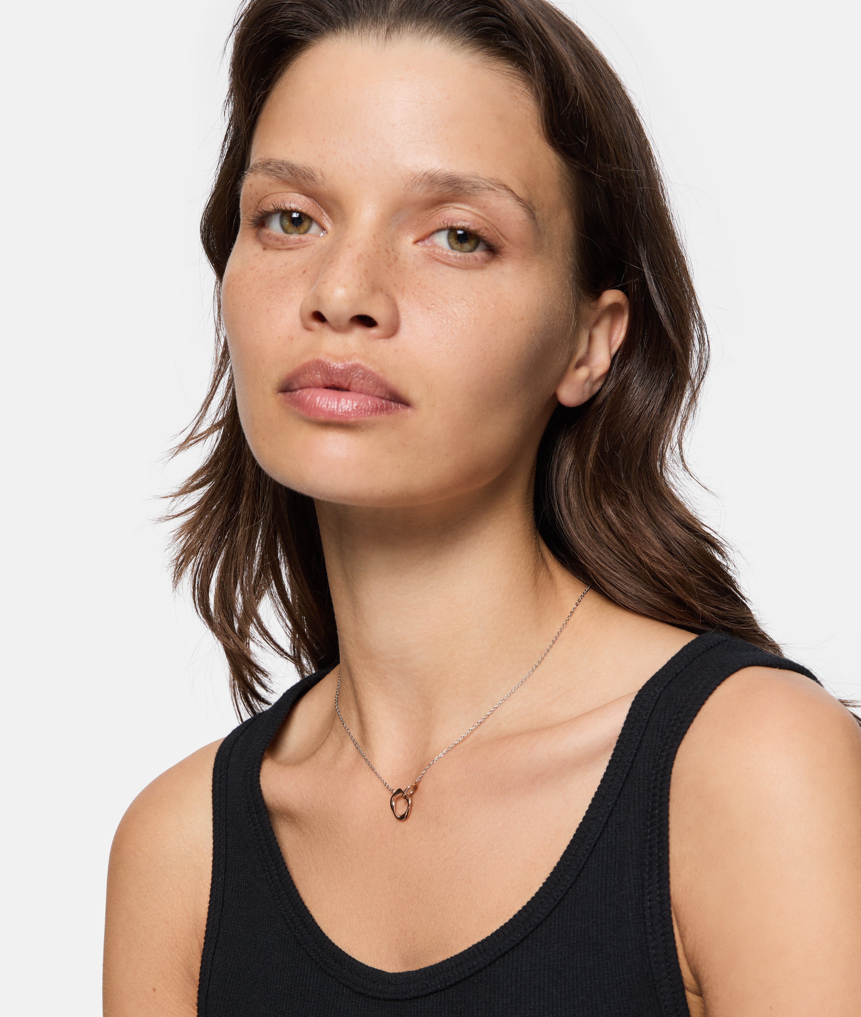 Frau mit mittelbraunem Haar in einem schwarzen Tanktop, die die LIEBESKIND BERLIN Halskette - The Organic Twist von Liebeskind Berlin für einen schicken Lagenlook trägt, schaut in die Kamera.