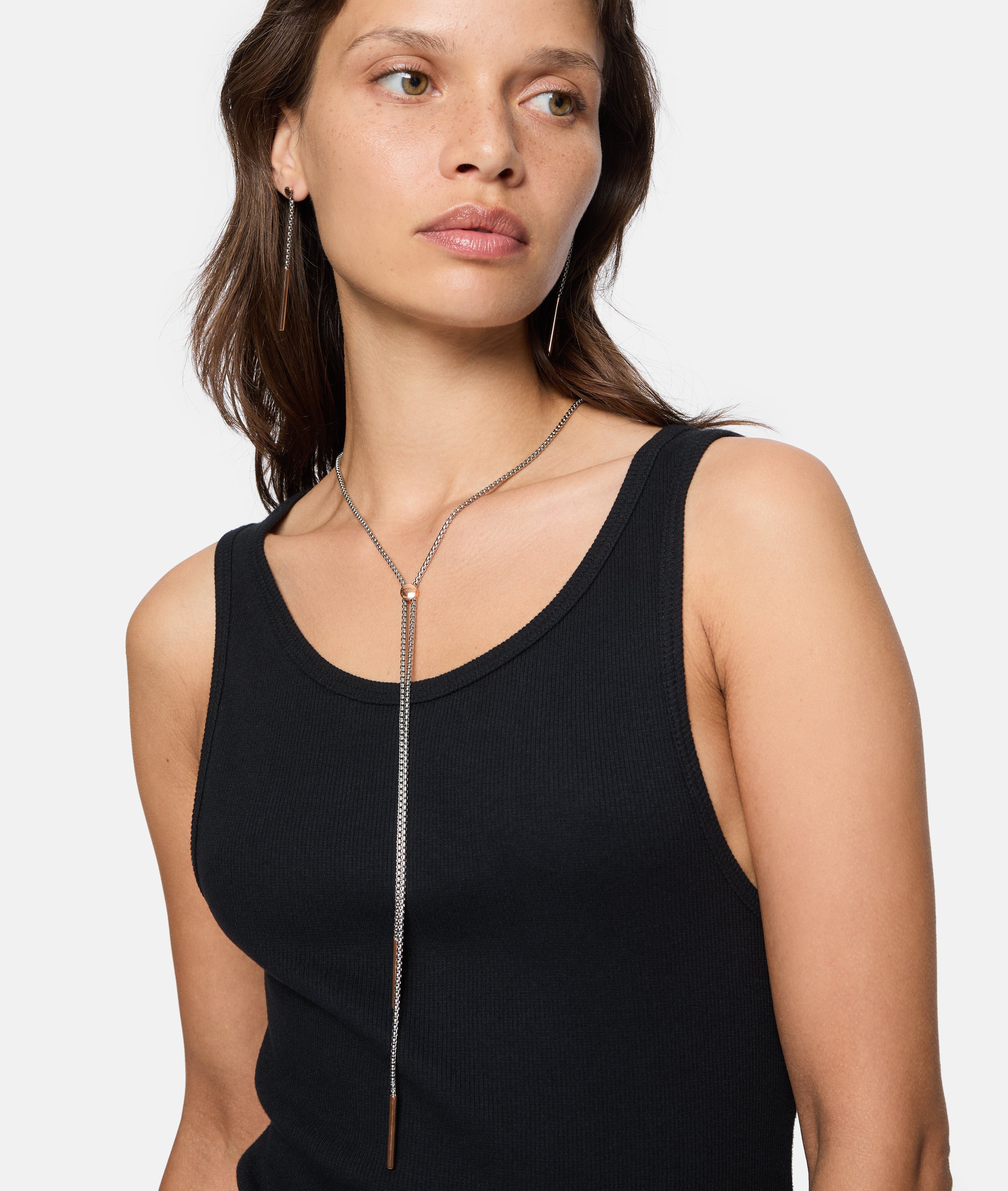 Frau in schwarzem Tank-Top trägt die Liebeskind Berlin Halskette - The Everyday Combination mit einem langen silbernen vertikalen Balkenanhänger.