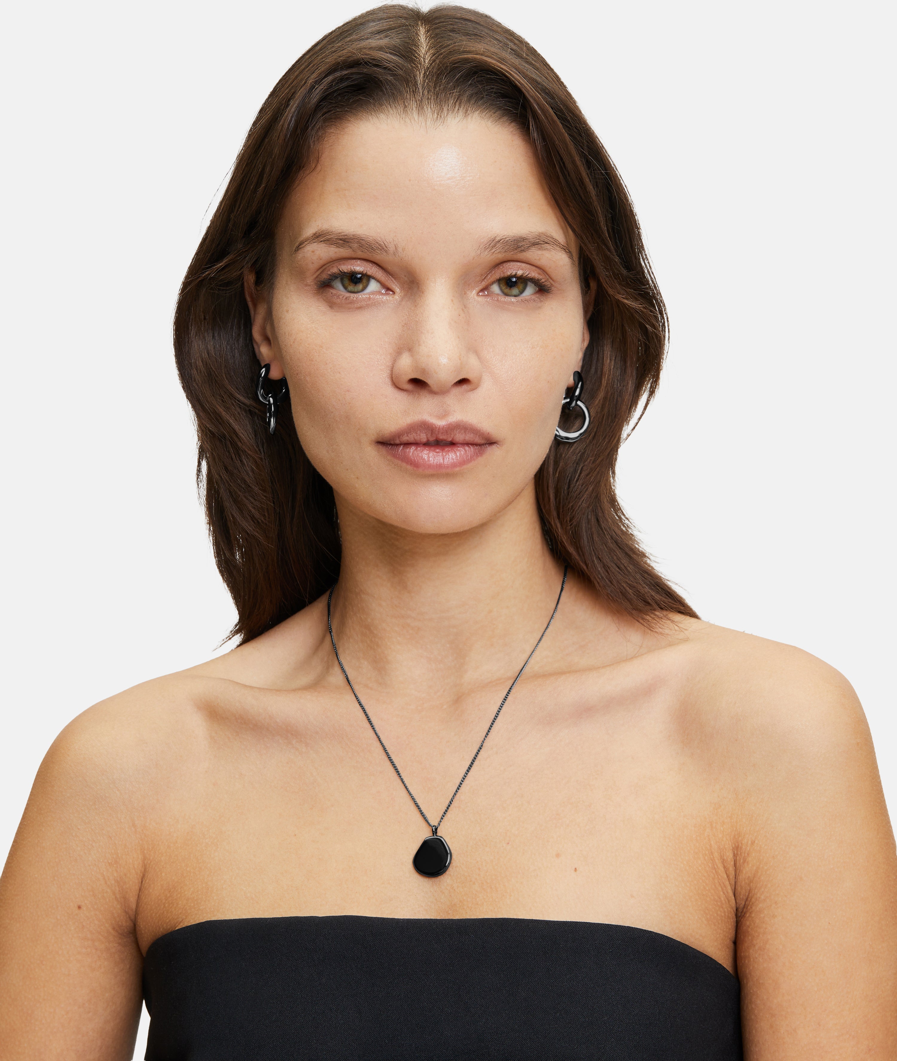 Frau mit glattem braunem Haar, trägt ein schwarzes trägerloses Top, silberne Ohrringe und die LIEBESKIND BERLIN Halskette - The Organic Pendant von Liebeskind Berlin.