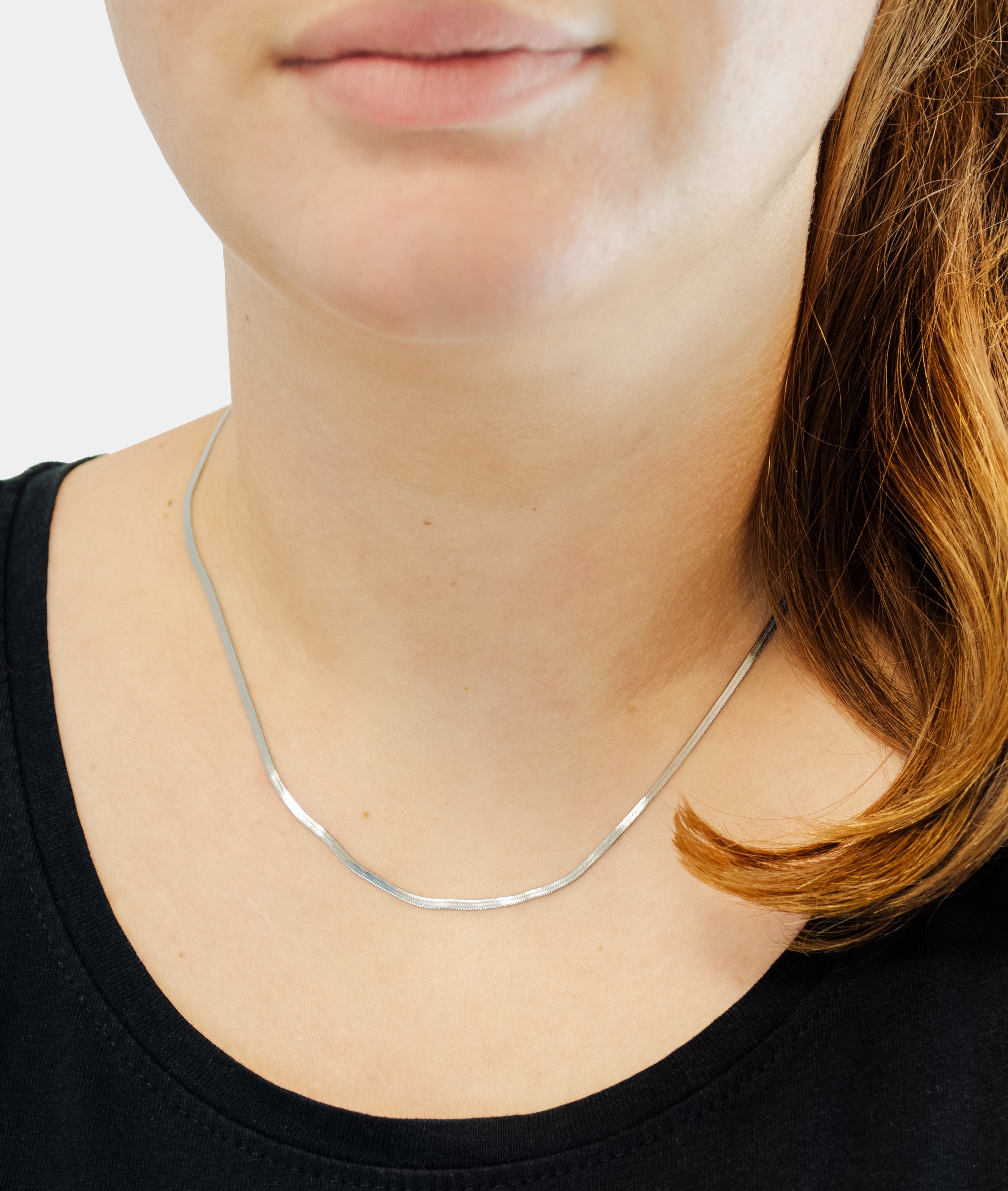 Eine Frau trägt die LIEBESKIND BERLIN Halskette - The Long Sleek, eine dünne silberne Halskette von Liebeskind Berlin, mit einem schwarzen Oberteil und ihr Haar elegant über eine Schulter drapiert.