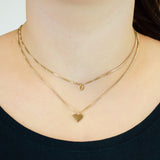 Eine Person trägt die Liebeskind Berlin Halskette - Layered Love: zwei goldene Halsketten, eine mit einem kleinen Kreisanhänger und die andere mit einem Herzanhänger.