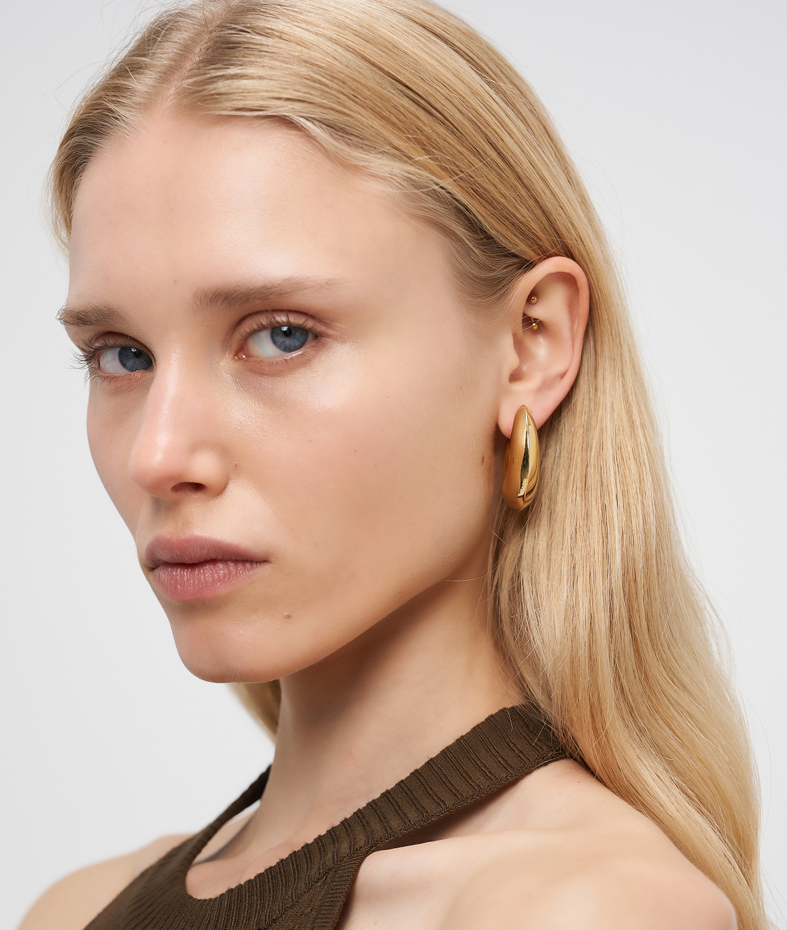 Frau mit langen blonden Haaren, die LIEBESKIND BERLIN Creole - Organic Shapes Ohrringe von Liebeskind Berlin und ein braunes Oberteil trägt, blickt in die Kamera und zeigt einen perfekten minimalistischen Stil.