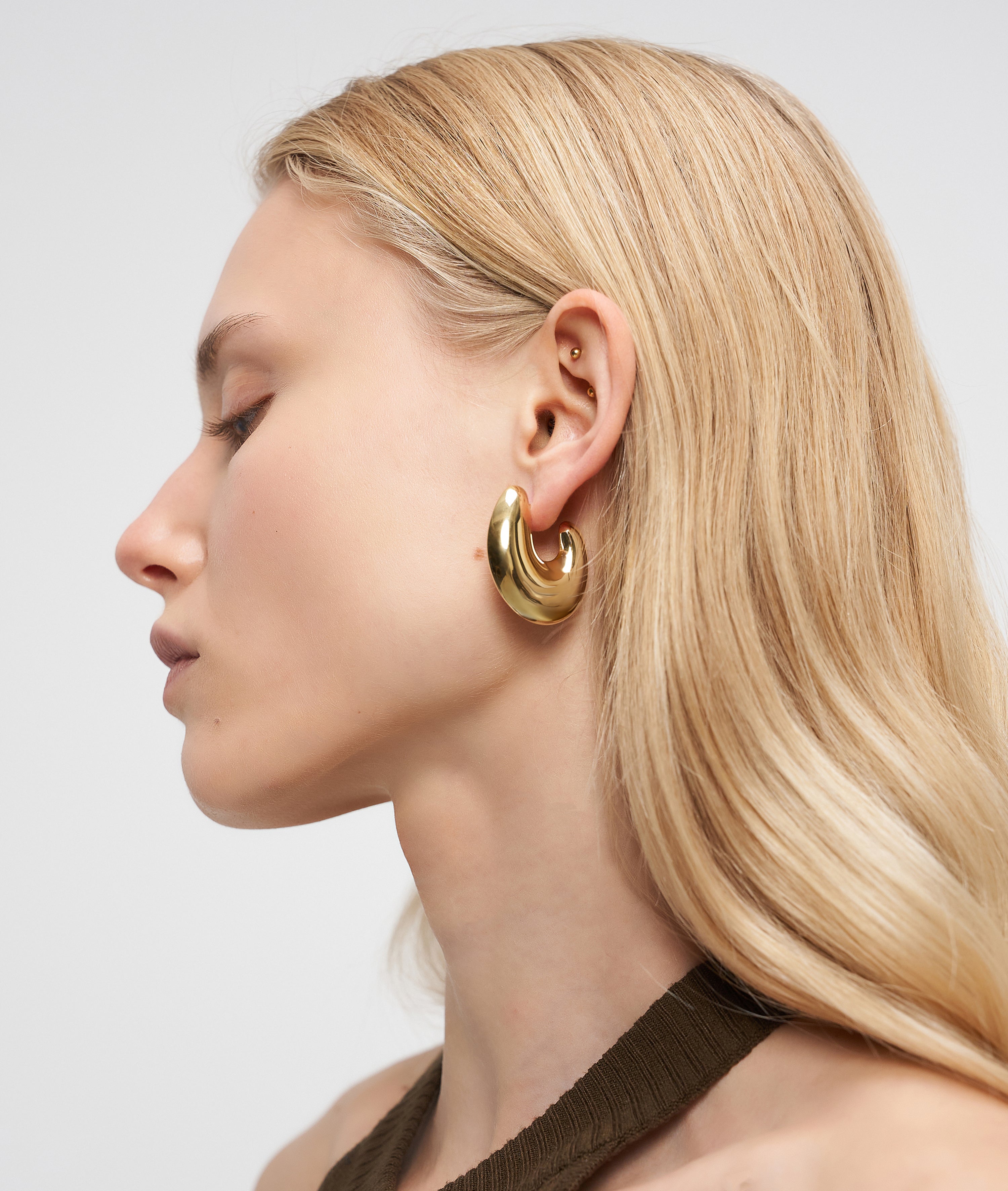 Frau mit langem blondem Haar trägt LIEBESKIND BERLIN Creole - Organic Shapes Goldohrringe von Liebeskind Berlin, dargestellt im Profil vor einem hellen Hintergrund.
