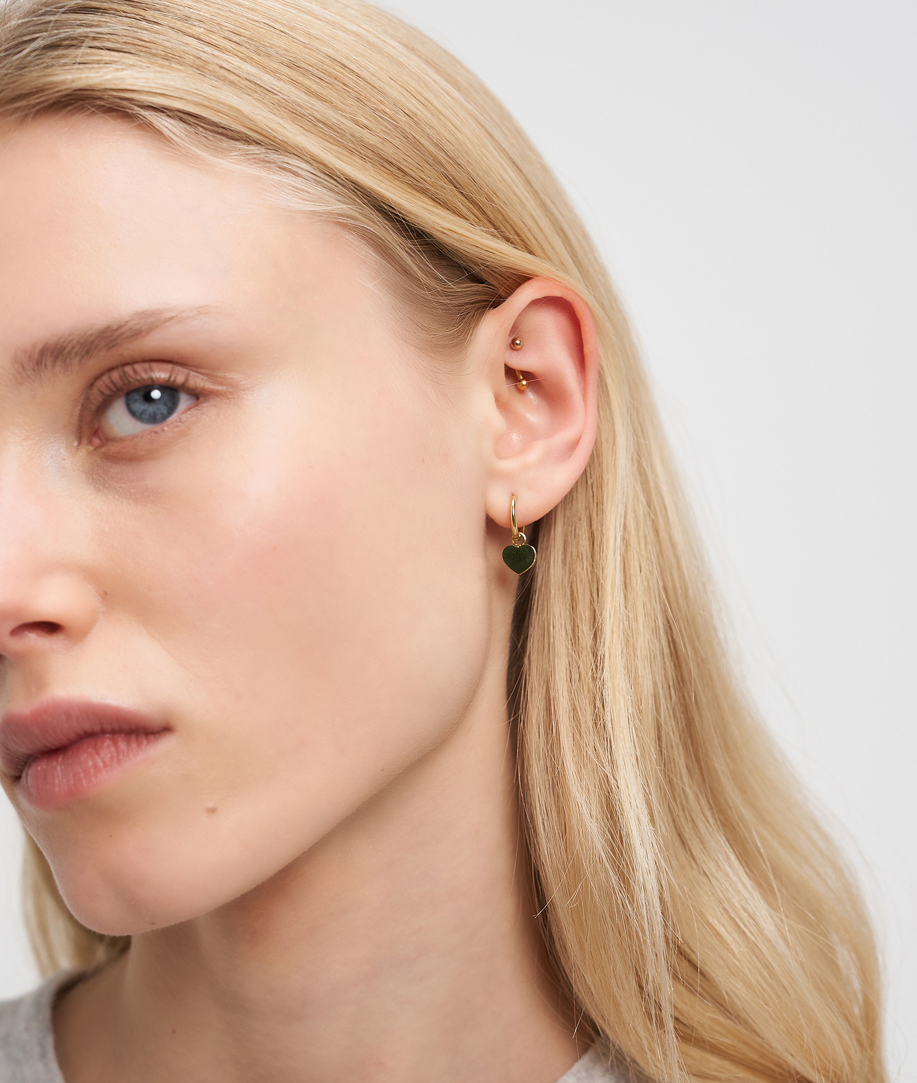 Nahaufnahme eines Frauengesichts mit blondem Haar, das Liebeskind Berlin Ohrring - My Heart Ohrringe und mehrere Ohrpiercings trägt.