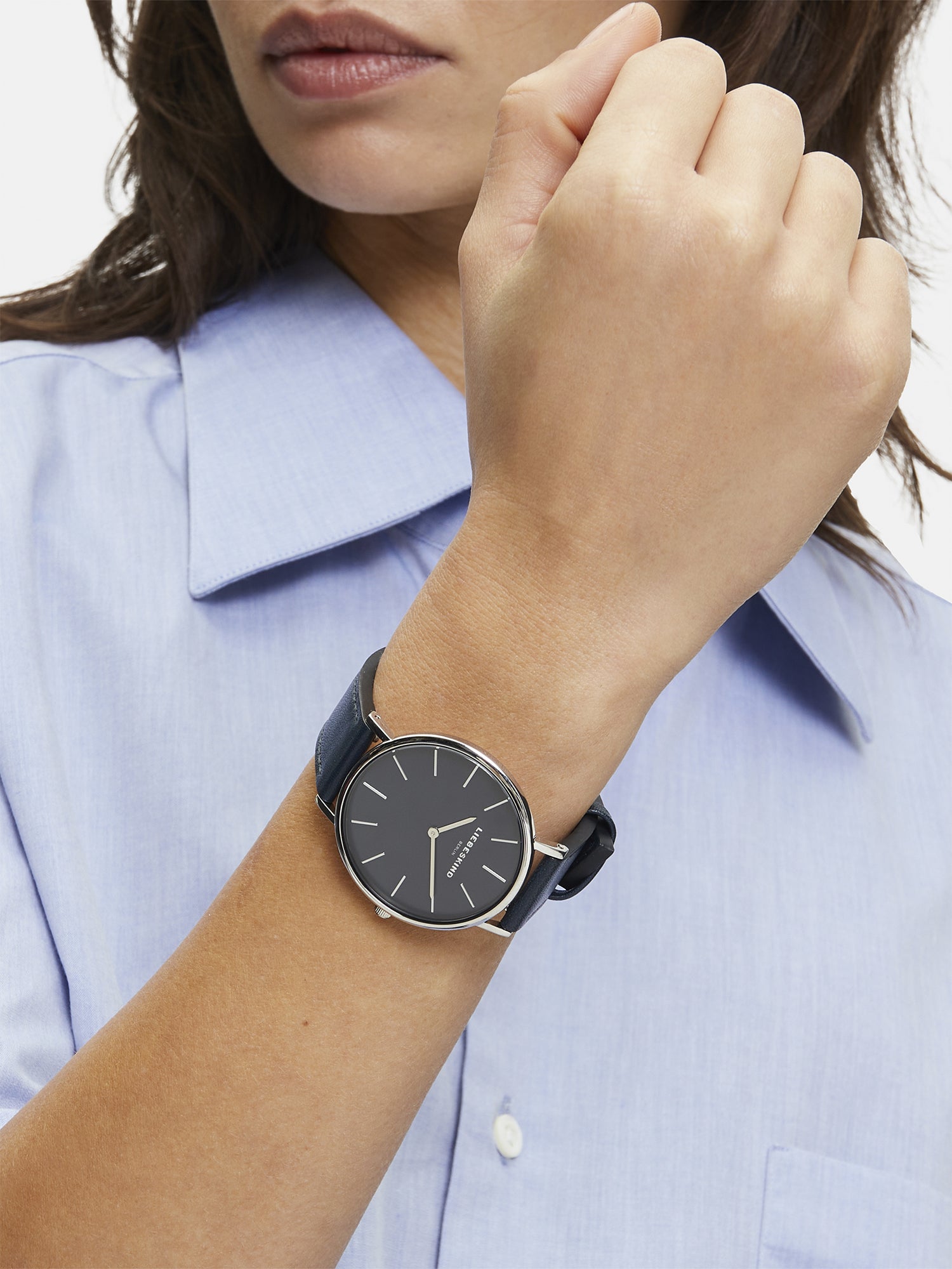 Eine Person in einem blauen Hemd trägt die LIEBESKIND BERLIN Armbanduhr - Skandinavian Classic von Liebeskind Berlin mit einem Lederriemen und hält die Faust erhoben neben dem Gesicht.