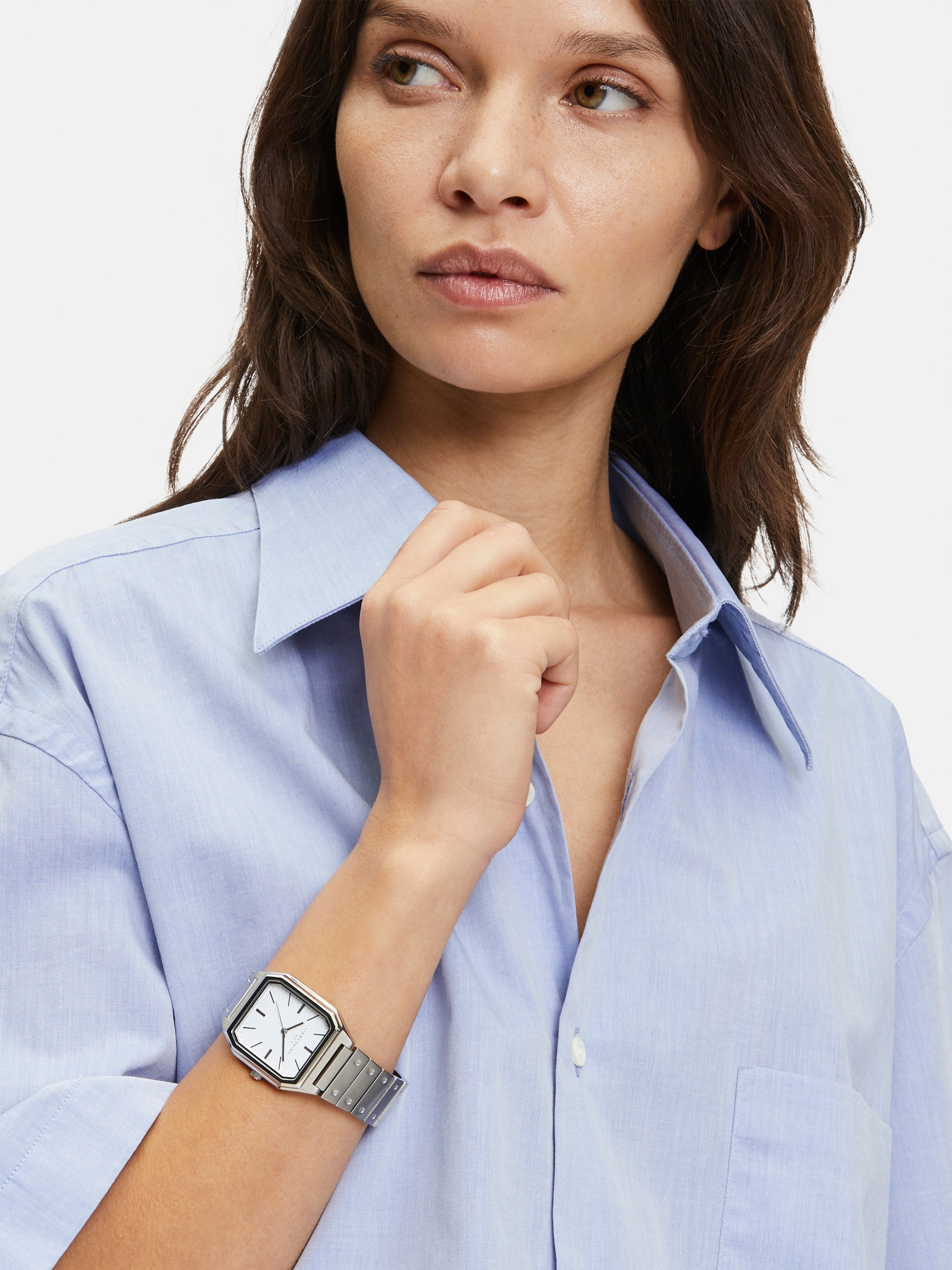 Frau in hellblauem Button-up-Hemd mit der LIEBESKIND BERLIN Armbanduhr - The Basic Staple von Liebeskind Berlin, Blick zur Seite.
