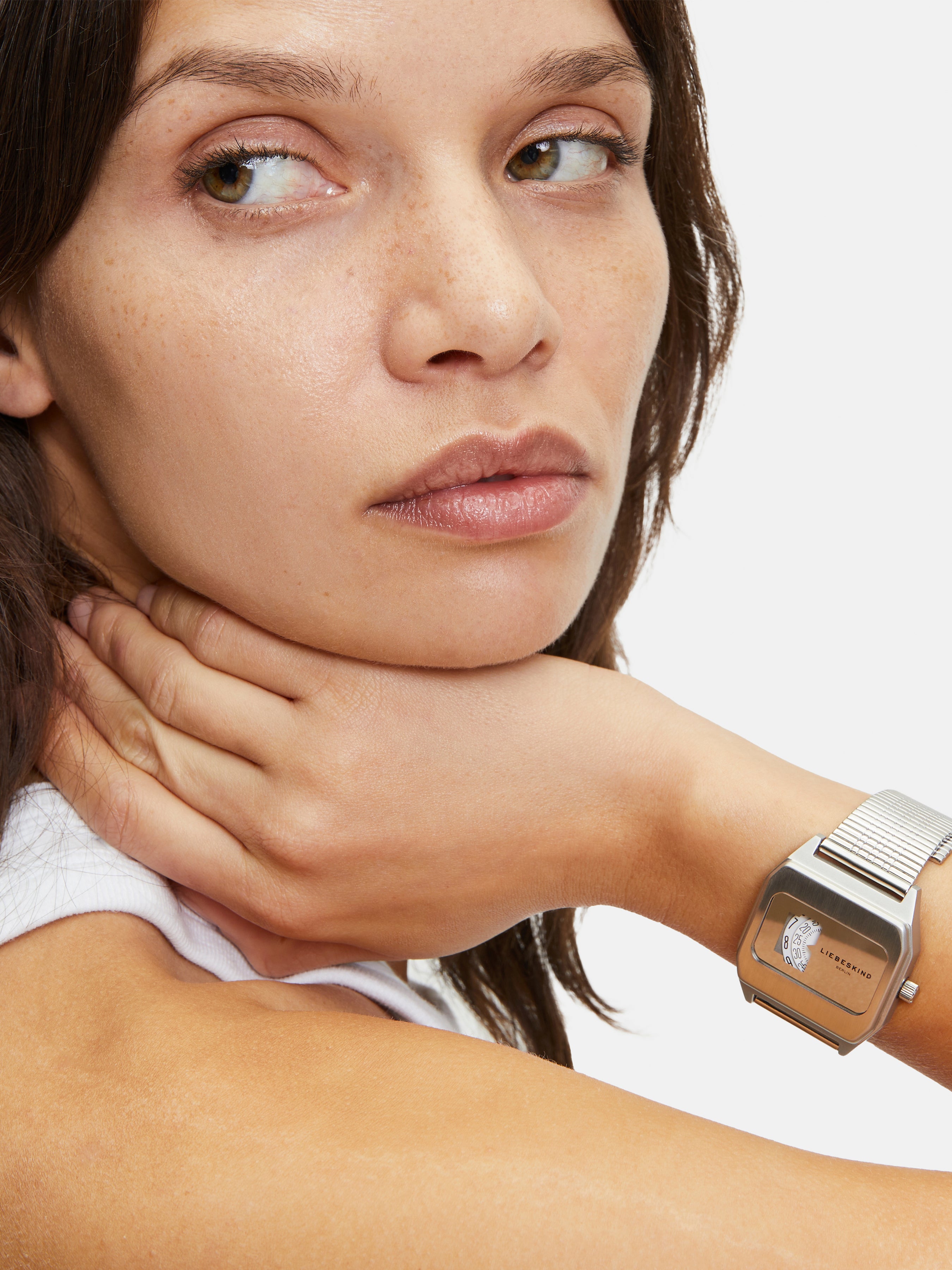 Eine Frau mit braunen Haaren schaut weg, das Kinn auf die Hand gestützt, sie trägt die LIEBESKIND BERLIN Armbanduhr - Vinyl Vision von Liebeskind Berlin mit einem eleganten Edelstahlgehäuse.