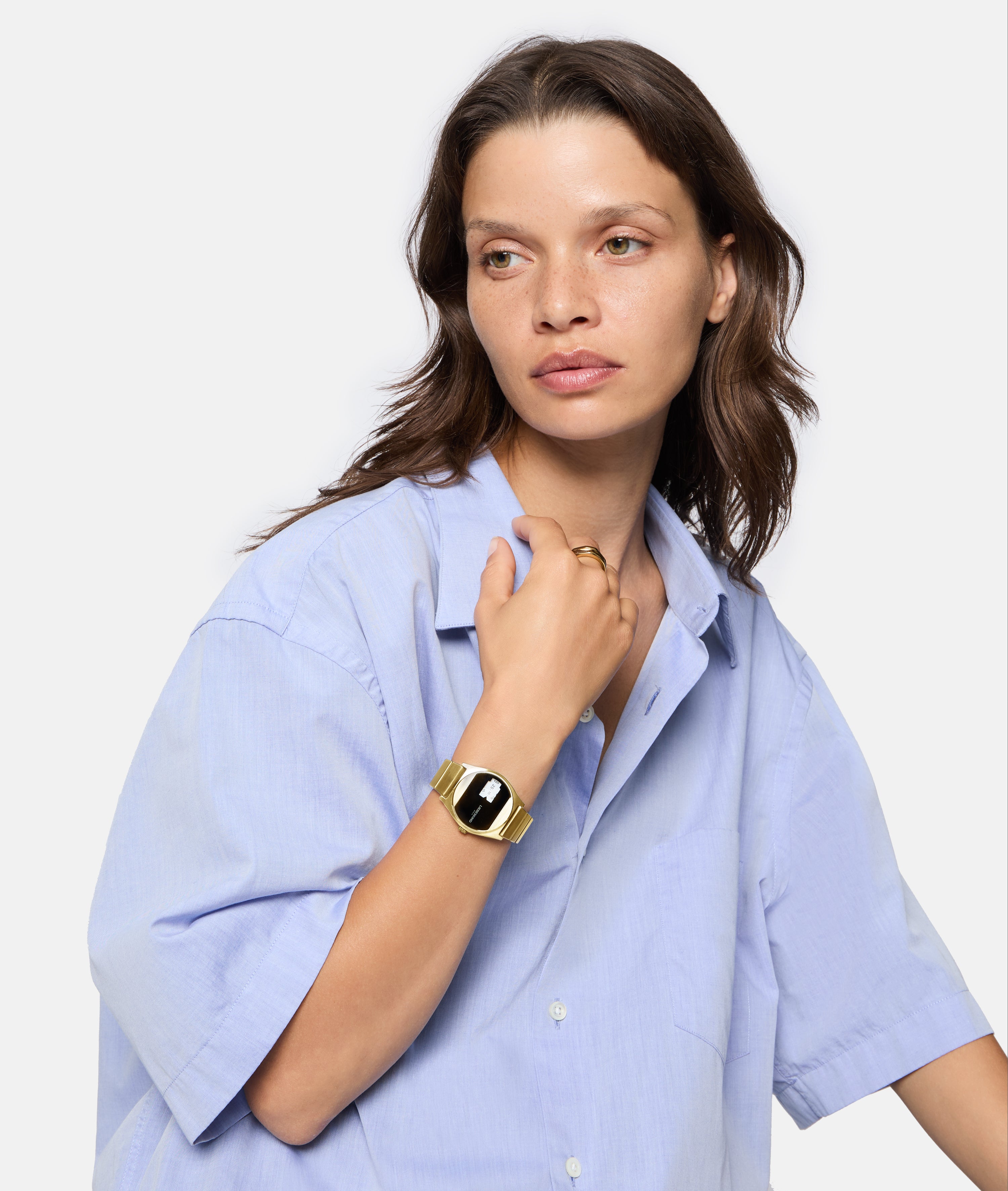 Frau in hellblauem Hemd trägt die LIEBESKIND BERLIN Armbanduhr - Round Vinyl Vision von Liebeskind Berlin mit verspiegeltem Ziffernblatt und einem Ring, während sie zur Seite blickt.