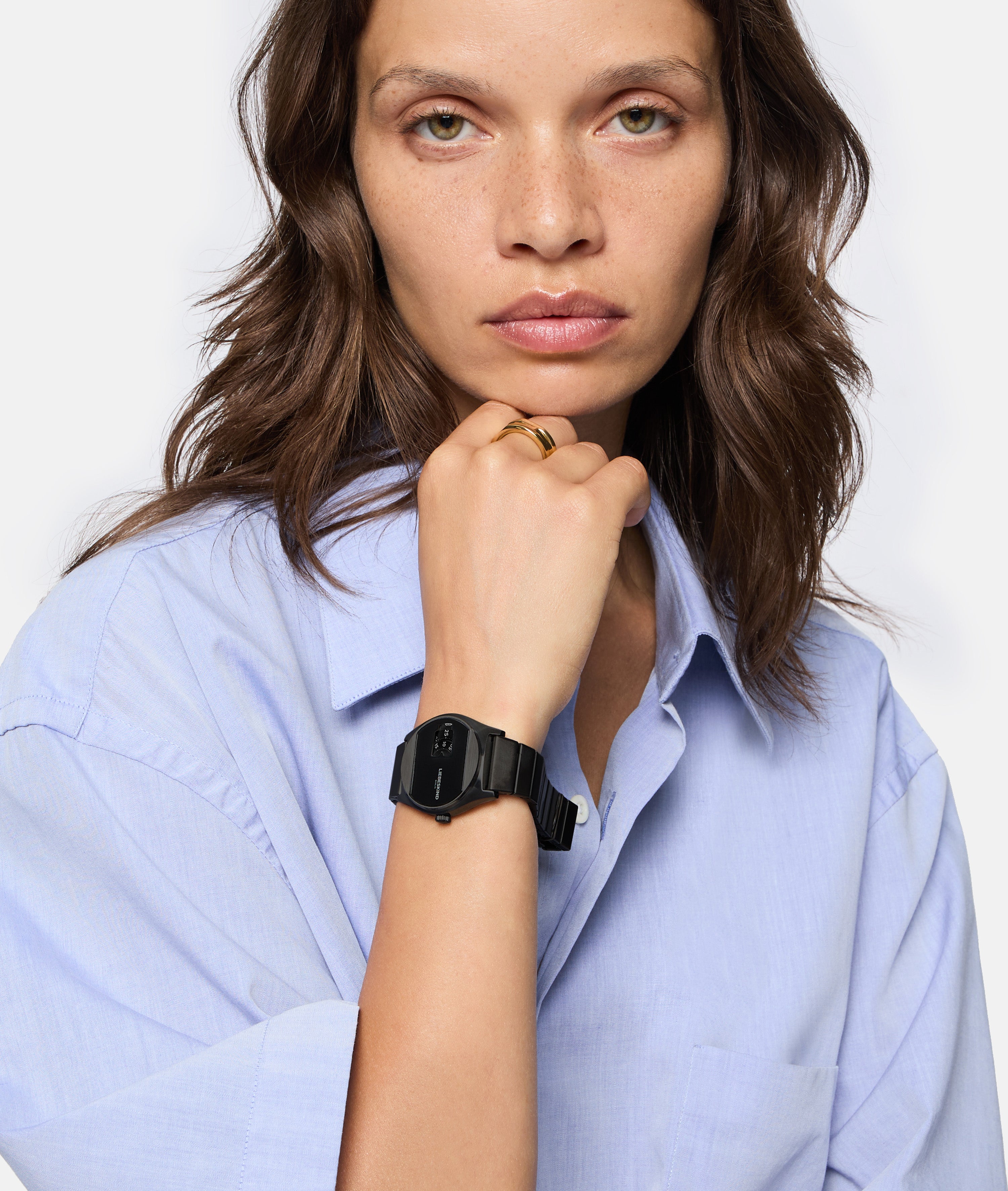 Eine Frau in einem hellblauen Hemd zeigt ihre Liebeskind Berlin Armbanduhr - Round Vinyl Vision, die Hand am Kinn und mit neutralem Gesichtsausdruck.