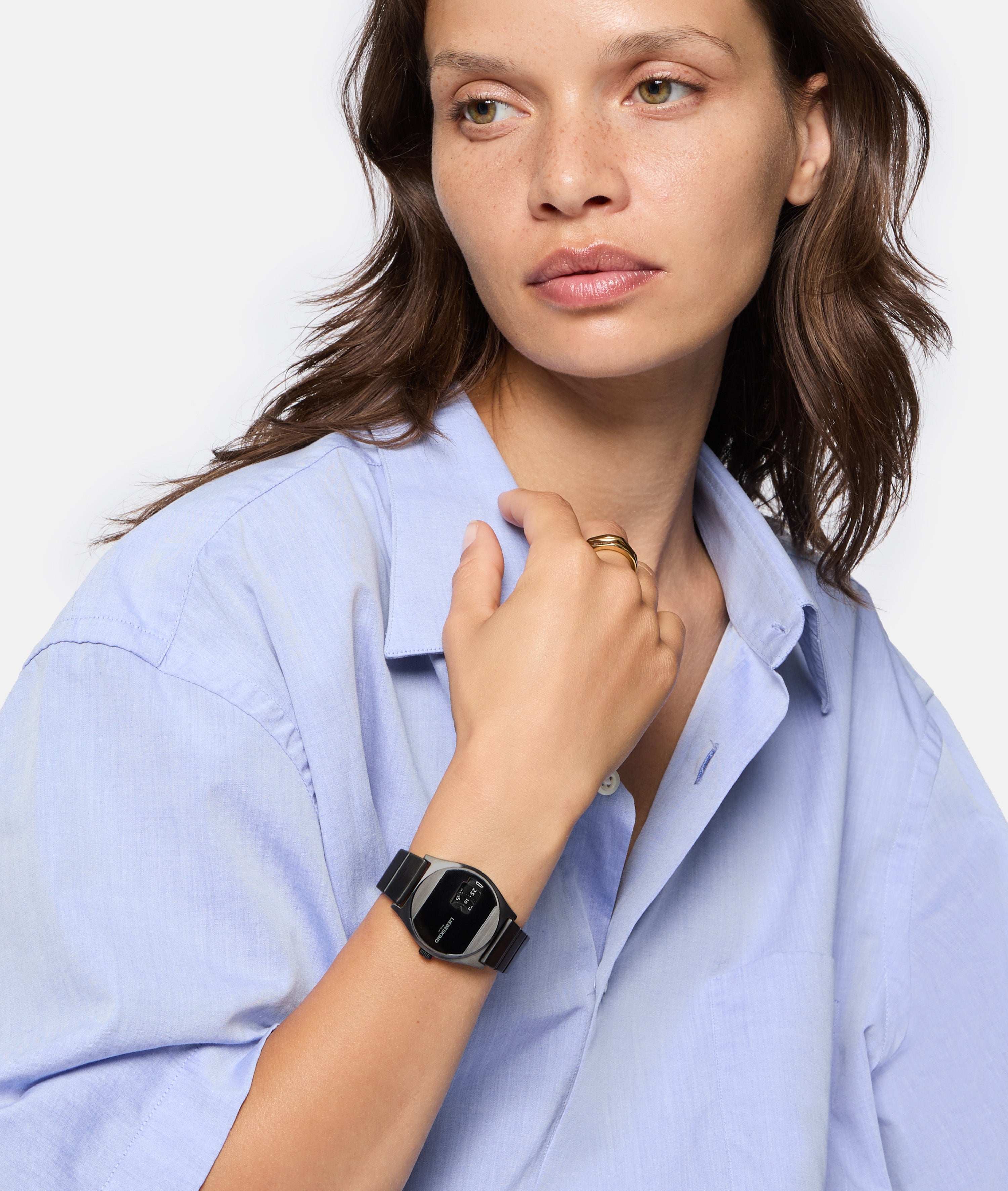 Eine Frau im hellblauen Hemd trägt die Liebeskind Berlin Armbanduhr - Round Vinyl Vision mit verspiegeltem Zifferblatt und blickt nachdenklich zur Seite.