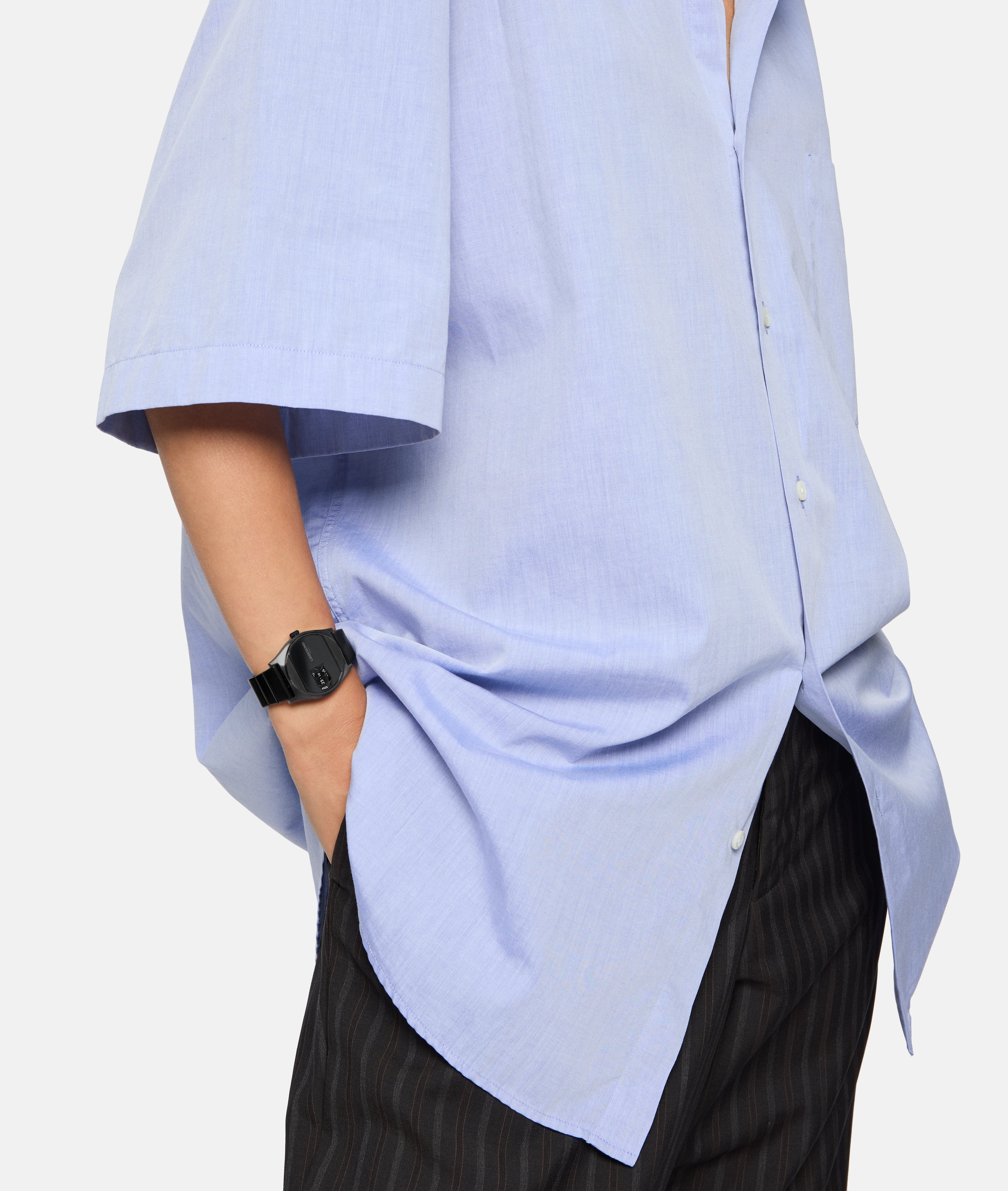 Eine Person in hellblauem Button-up-Hemd und Nadelstreifenhose trägt die Liebeskind Berlin Armbanduhr - Round Vinyl Vision mit verspiegeltem Ziffernblatt, die Hand stilvoll in die Tasche gesteckt.