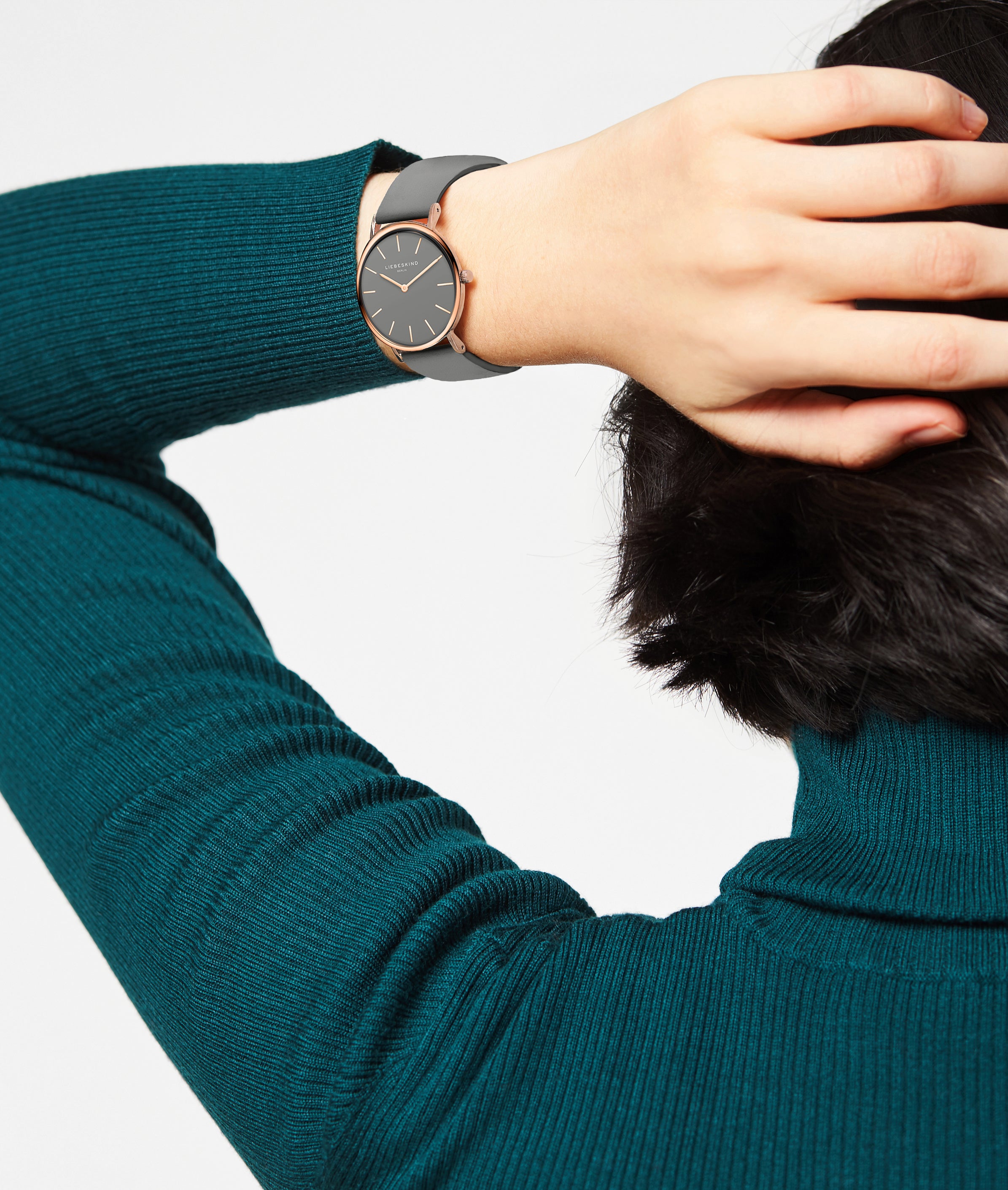 Eine Person in einem blaugrünen Pullover zeigt die LIEBESKIND BERLIN Armbanduhr - The Modern Must-Have von Liebeskind Berlin und hält ihre Hand hinter den Kopf.