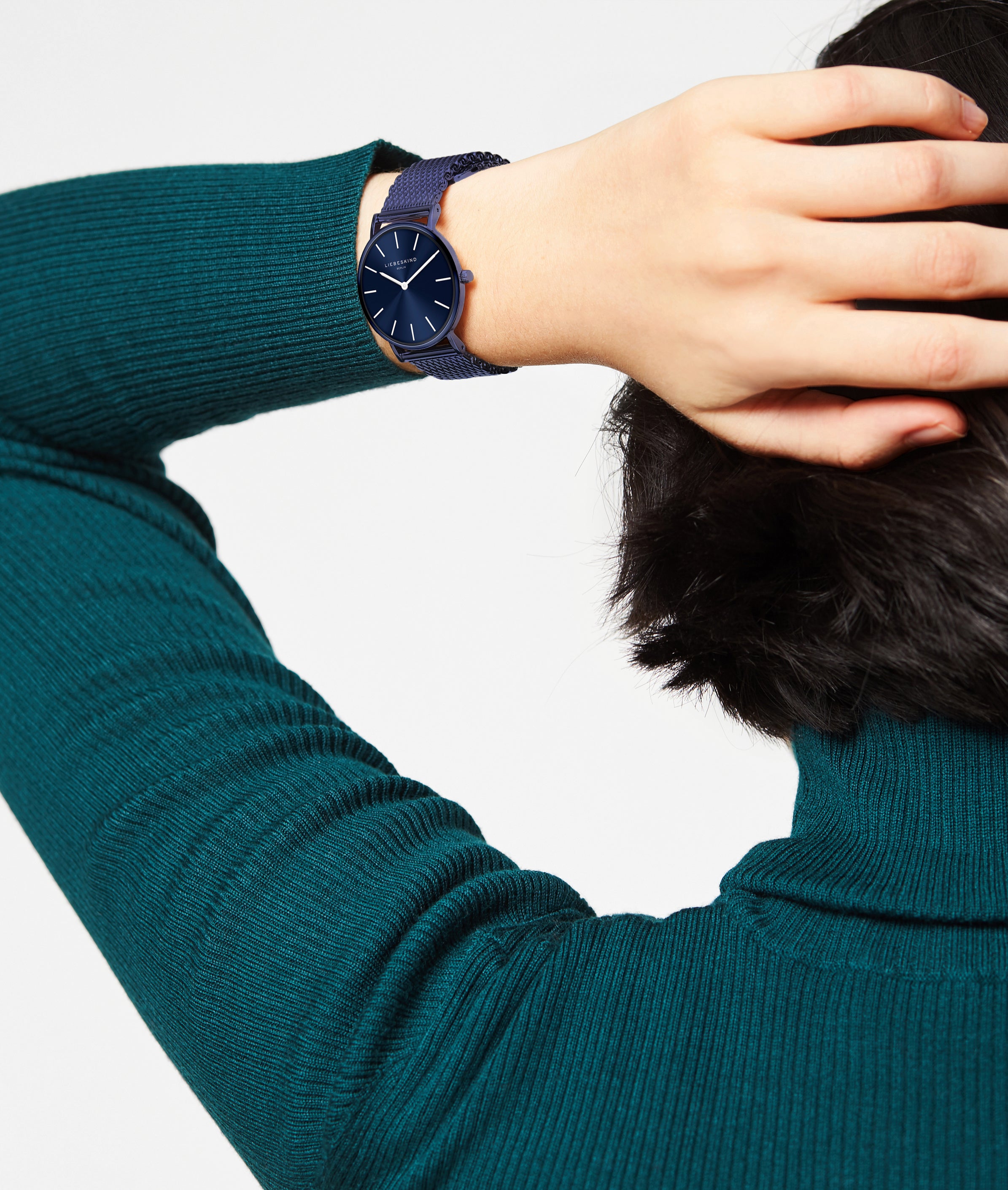 Person mit grünem Rippenpulli, die den Kopf berührt und die Liebeskind Berlin Color Up Armbanduhr trägt.
