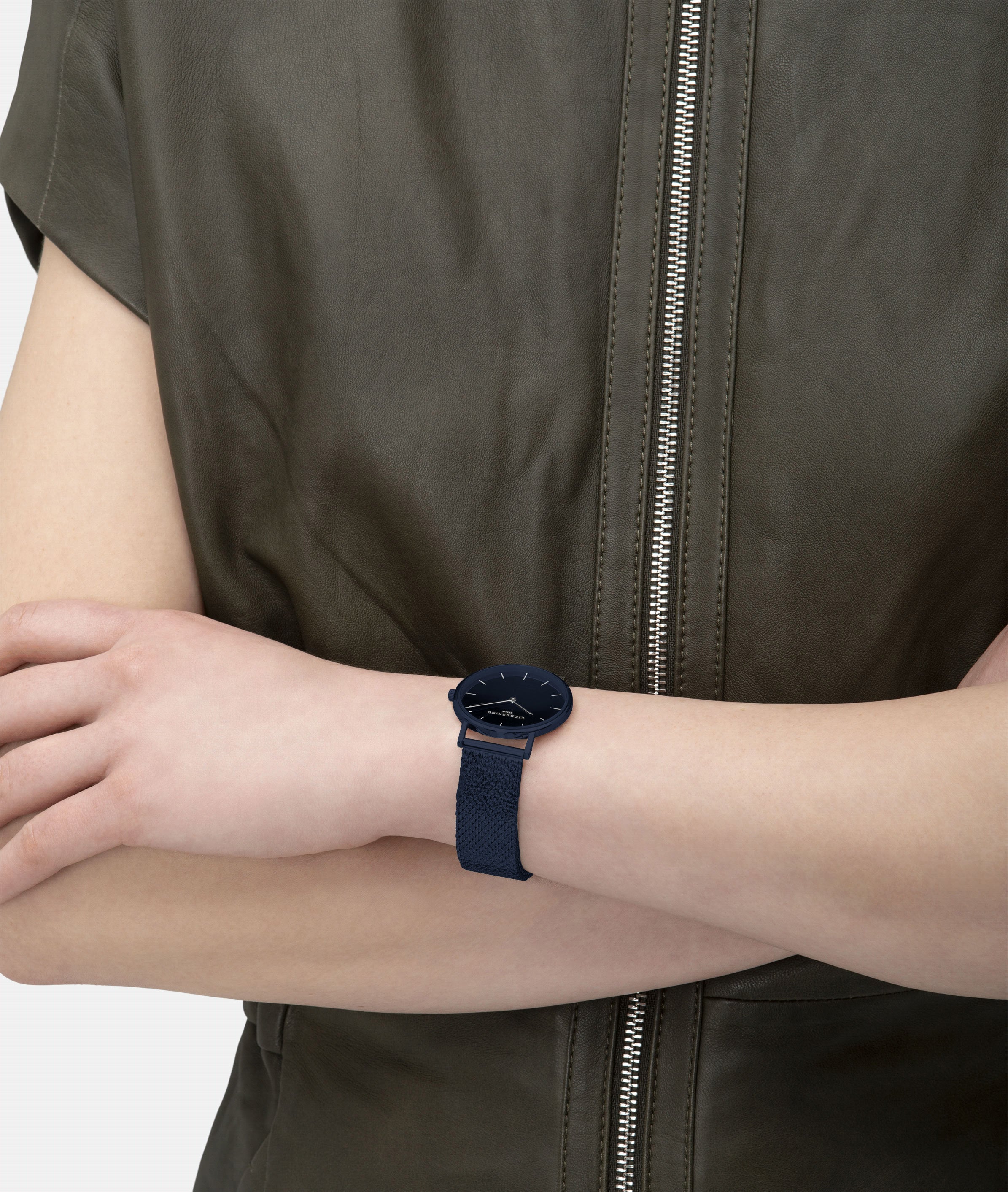Person trägt eine ärmellose Jacke mit Reißverschluss und eine LIEBESKIND BERLIN Armbanduhr - Glitter-Special von Liebeskind Berlin mit Edelstahl-Meshband und minimalistischem Design am linken Handgelenk.