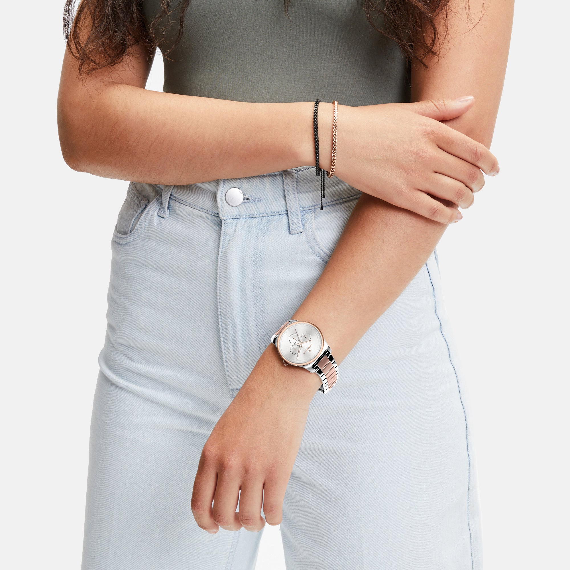 Frau in hellen Jeans und grünem Oberteil, die eine Liebeskind Berlin Classic x Trends Armbanduhr und ein Armband trägt, verschränkt lässig die Arme.