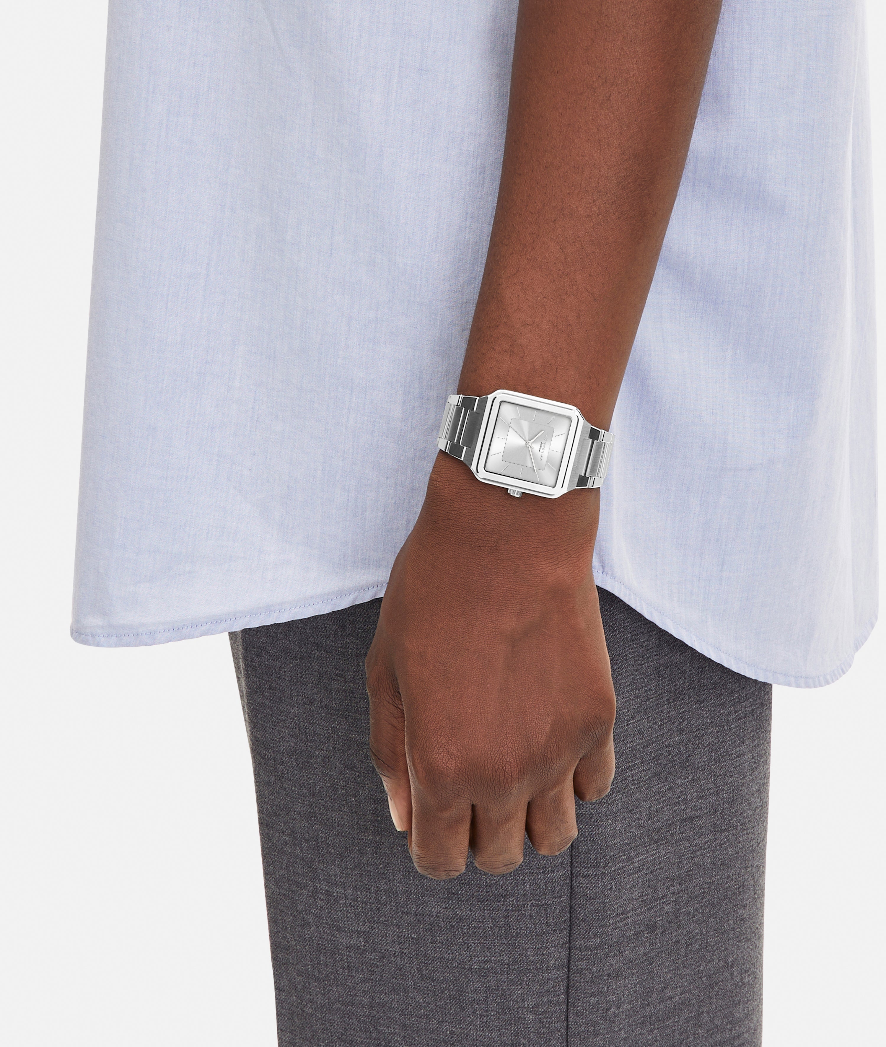 A person in a light blue shirt and gray pants wears the LIEBESKIND BERLIN Armbanduhr – The Square Minimalist on their left wrist, arm relaxed at their side, against a plain background.