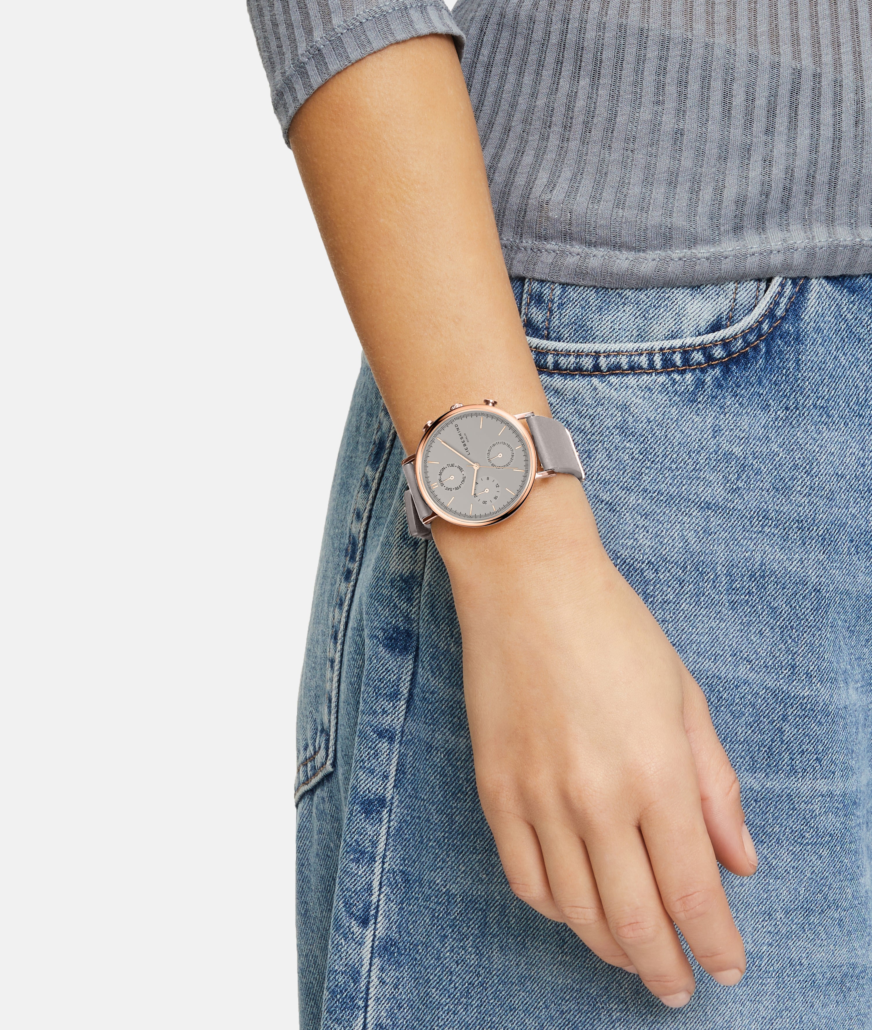 Eine Person in Jeans und einem gerippten Oberteil trägt die LIEBESKIND BERLIN Armbanduhr - The Multi-Function von Liebeskind Berlin, mit einem runden Gesicht und grauem Band.