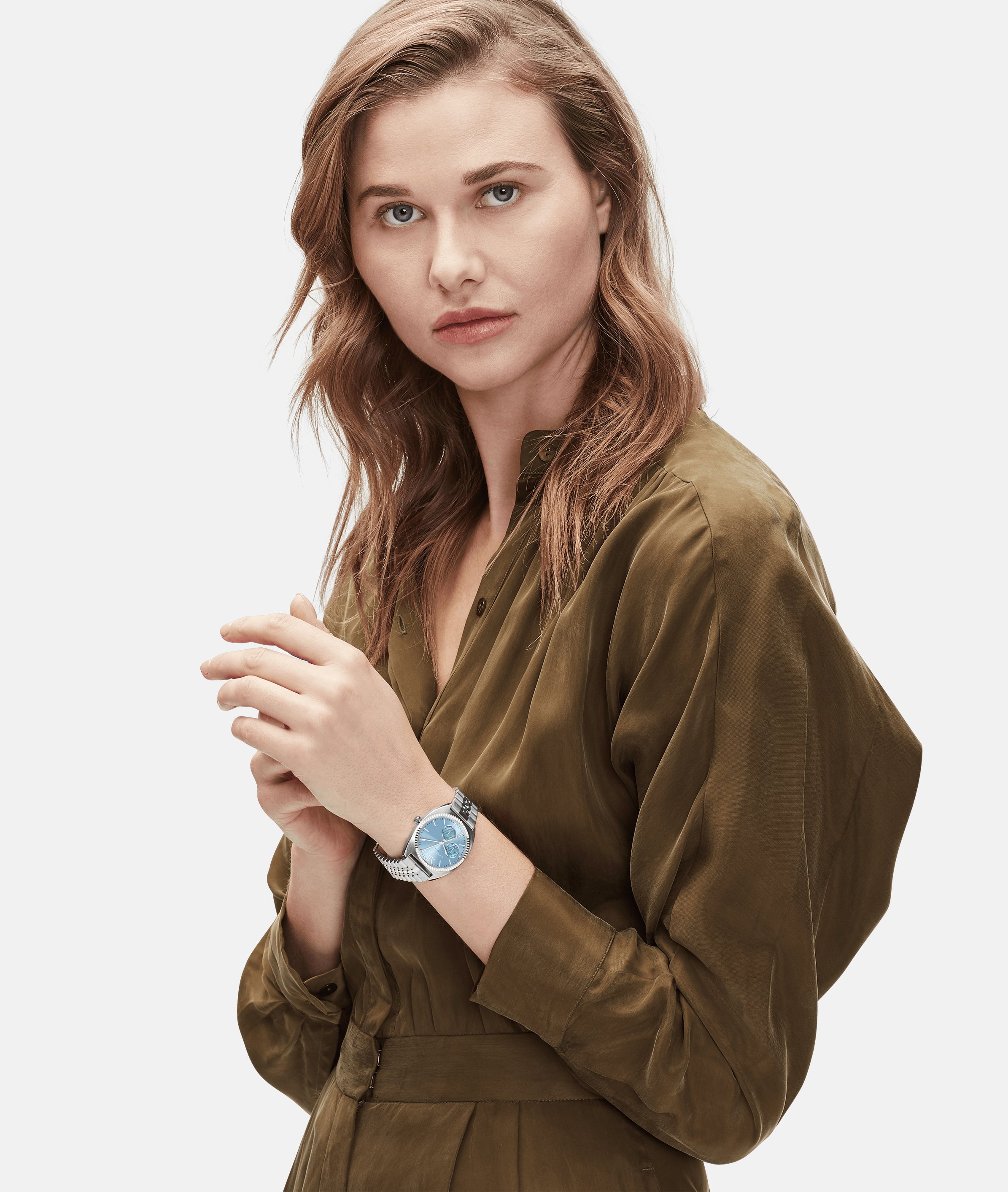 Frau im olivgrünen Kleid trägt die LIEBESKIND BERLIN Armbanduhr - The Colorful Multifunction von Liebeskind Berlin mit Edelstahlarmband, während sie mit neutralem Blick in die Kamera schaut.