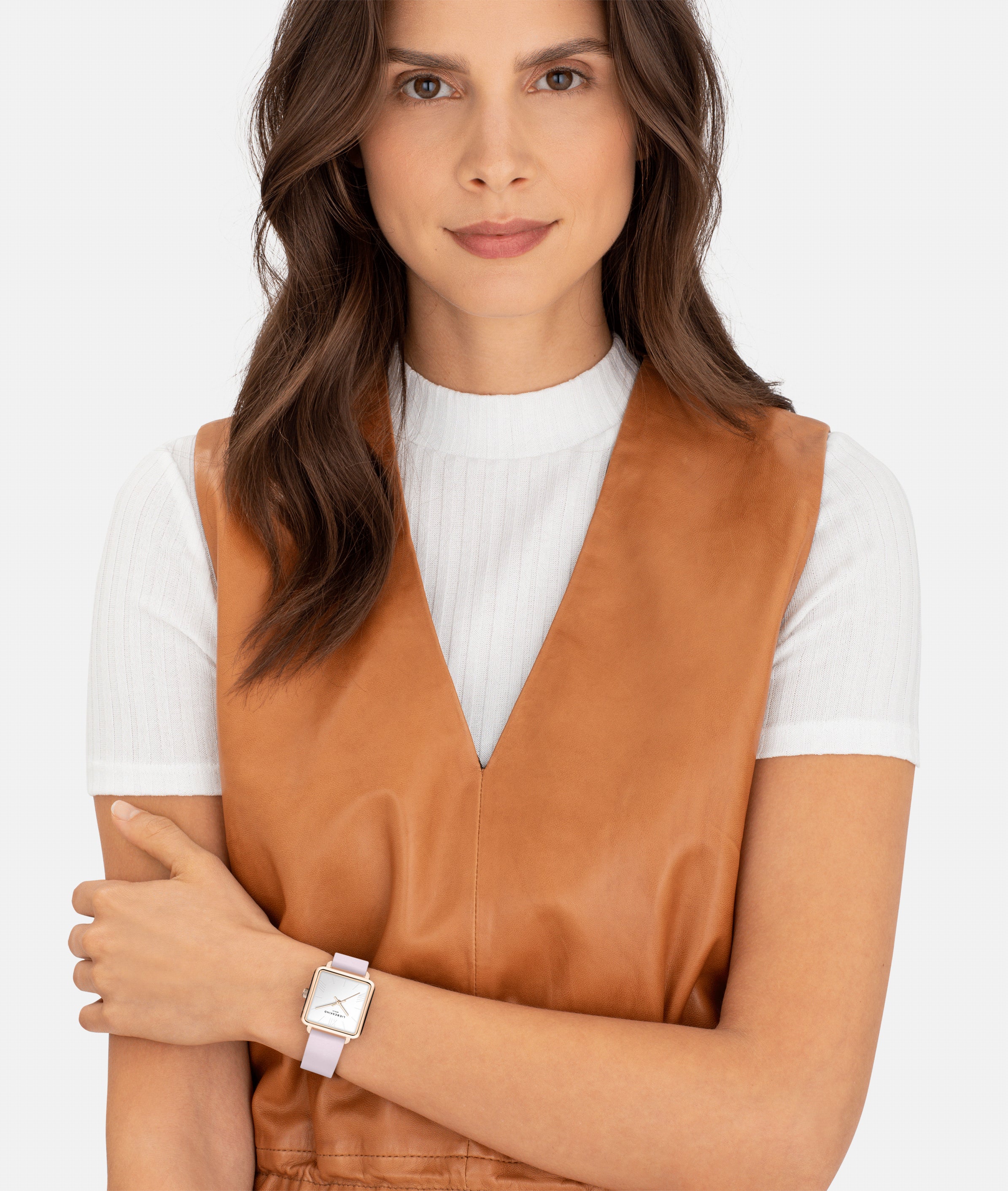 Frau mit gewellten braunen Haaren trägt eine braune Weste, ein weißes Oberteil und die LIEBESKIND BERLIN Armbanduhr - The Classic Square von Liebeskind Berlin, die sich durch skandinavisch inspiriertes Design auszeichnet.
