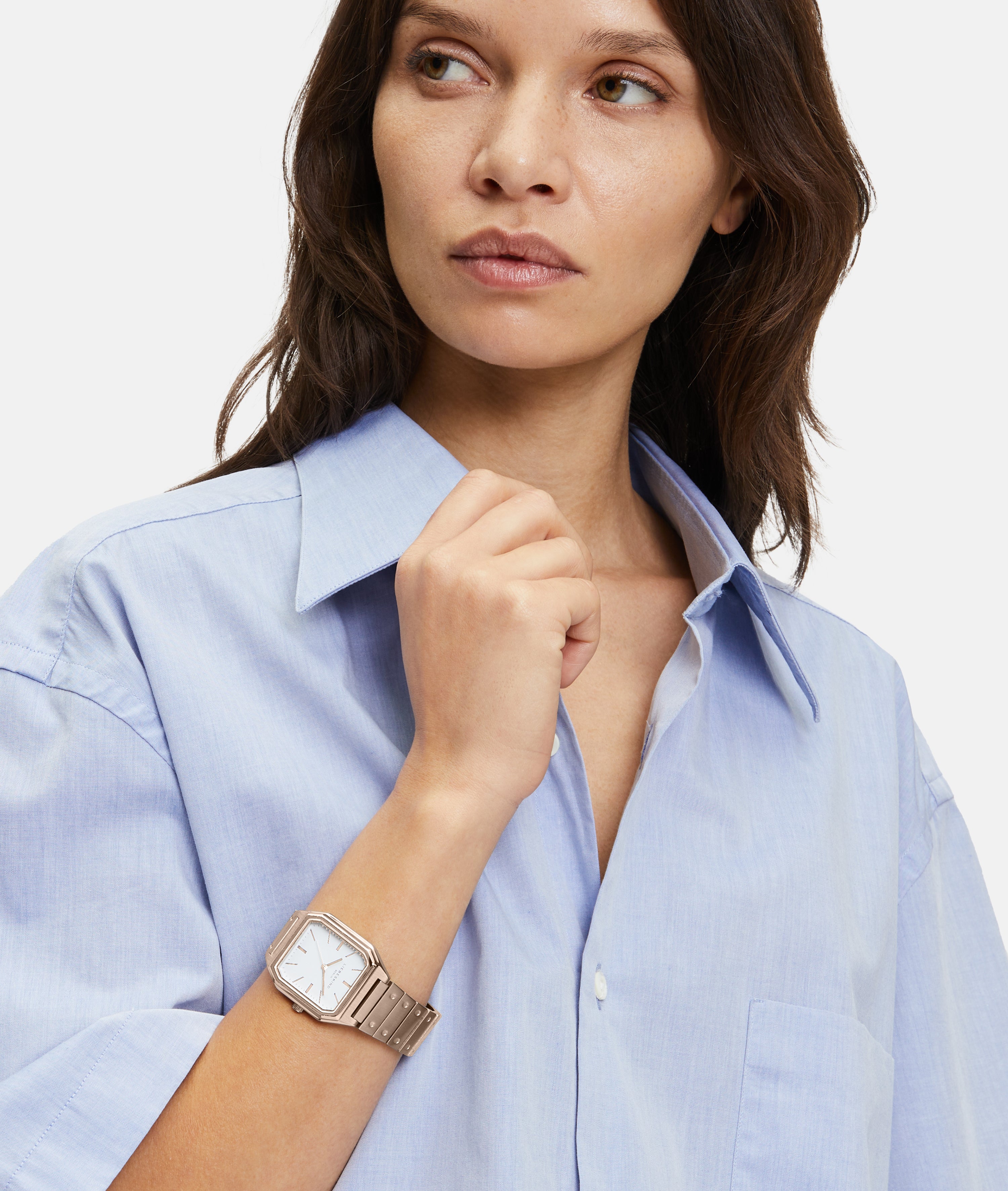 Eine Frau im hellblauen Button-up-Hemd trägt die Liebeskind Berlin Armbanduhr - The Modern Staple mit rechteckigem Gehäuse, während sie zur Seite schaut.