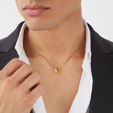 Ein Mann trägt die Philipp Plein Halskette - PLEIN CUFF Goldkette von Philipp Plein, kombiniert mit einem schwarzen Blazer und einem weißen Hemd.