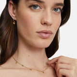 Eine Frau mit hellen Augen trägt goldene Creolen Creole - Flower von Tamaris mit zarten Zirkonia und eine zierliche goldene Halskette von Tamaris mit kleinen Anhängern.