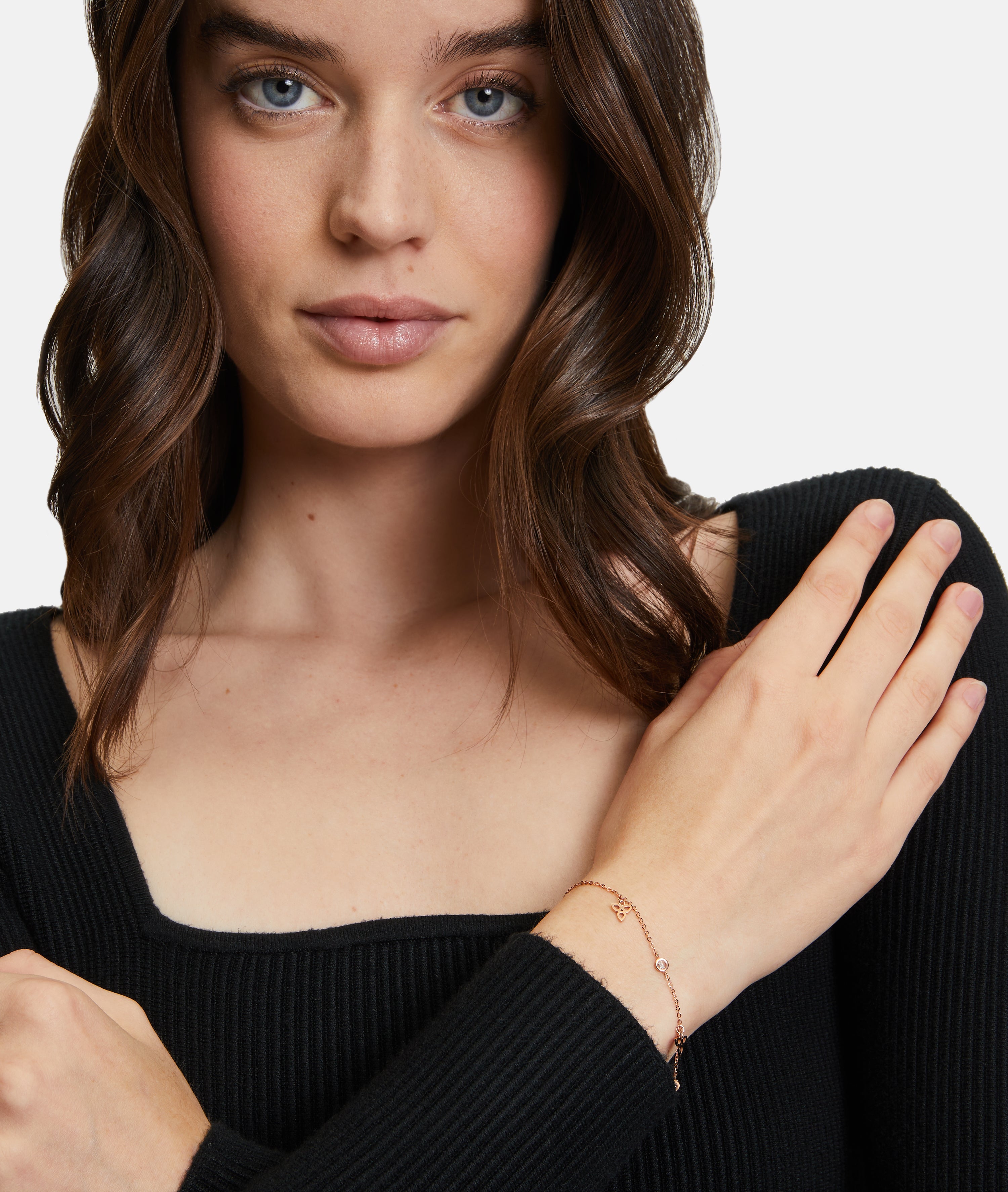 Eine Frau in einem schwarzen Oberteil trägt das Tamaris Armband - Flower an ihrem linken Handgelenk und posiert mit der Hand auf ihrer Schulter.